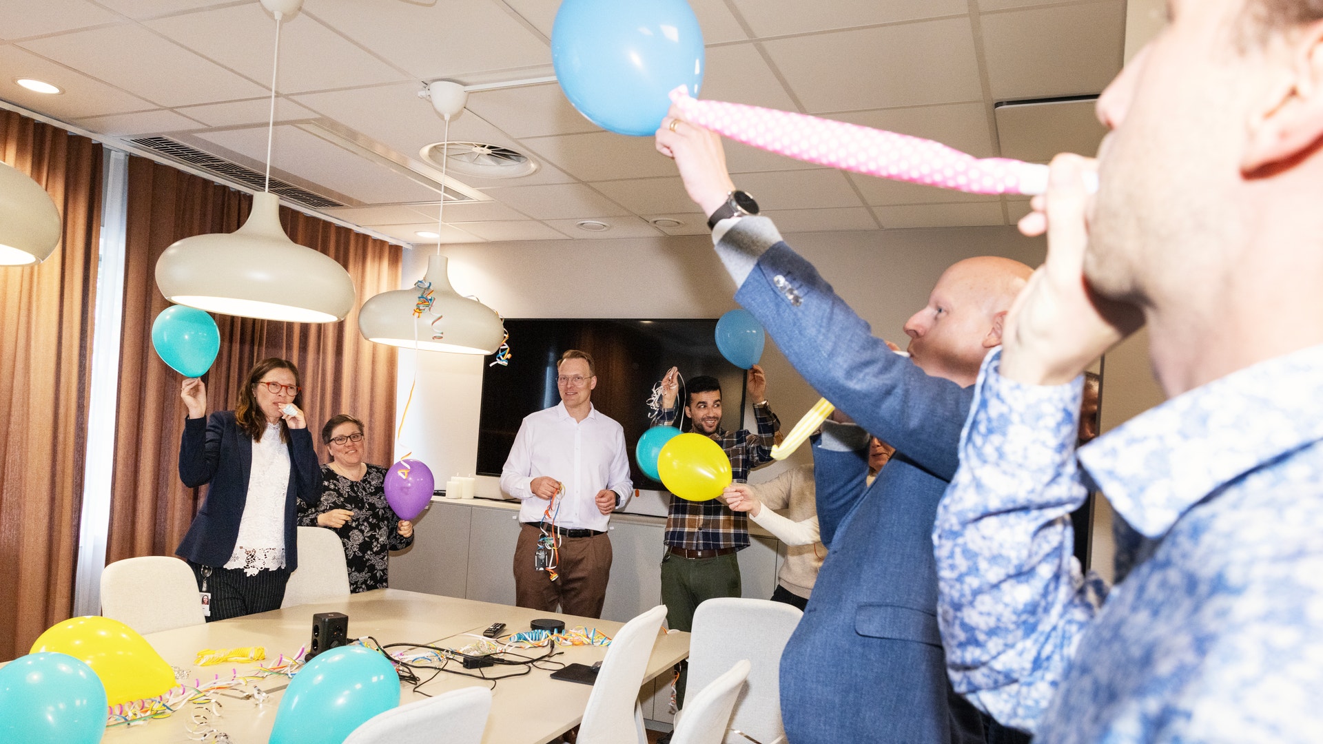 Kollegor firar tillsammans i ett konferensrum med ballonger och konfetti på bordet.
