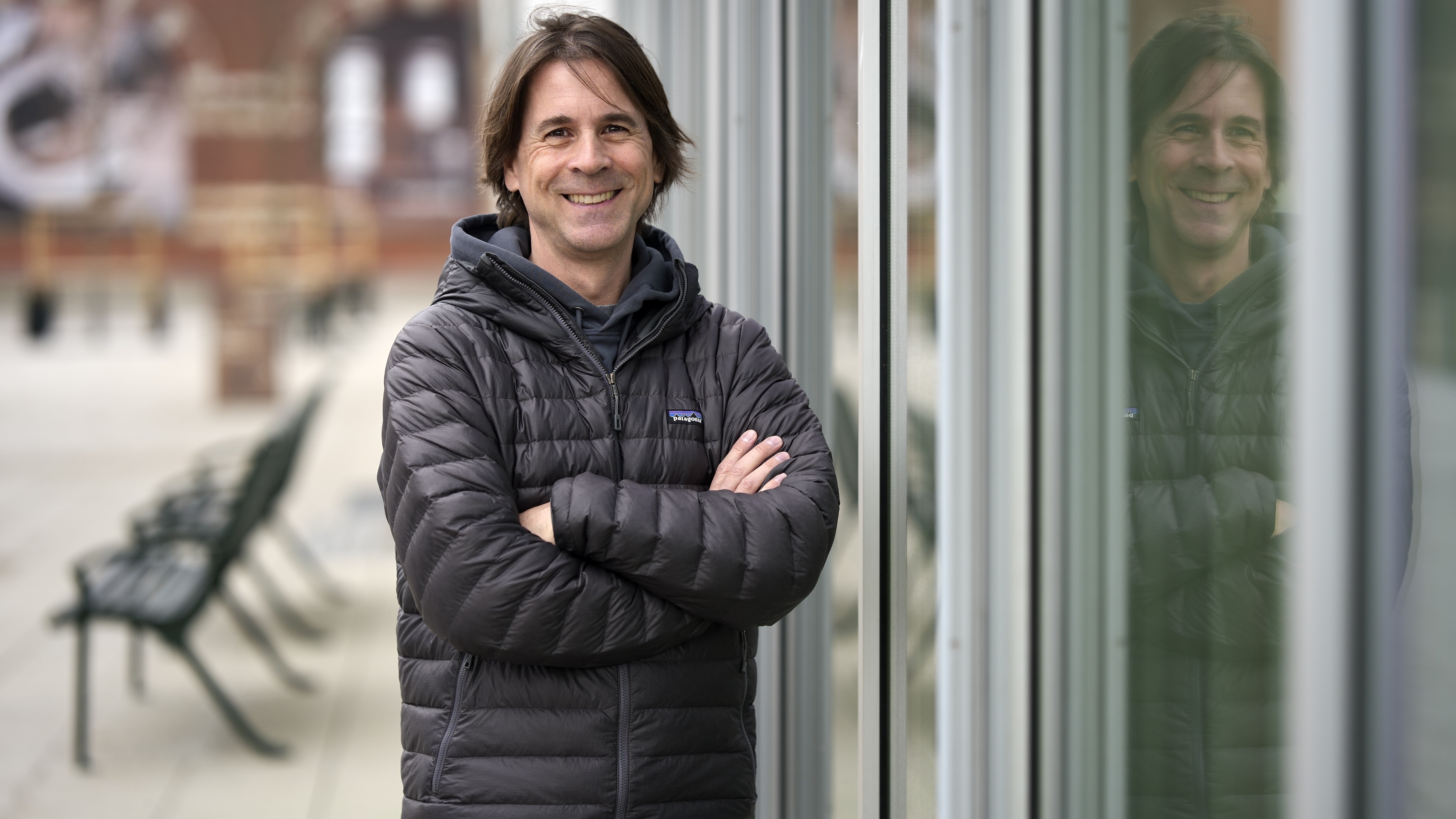 Porträttfoto av en man i svart dunjacka som står utomhus med armarna i kors och ler mot kameran.