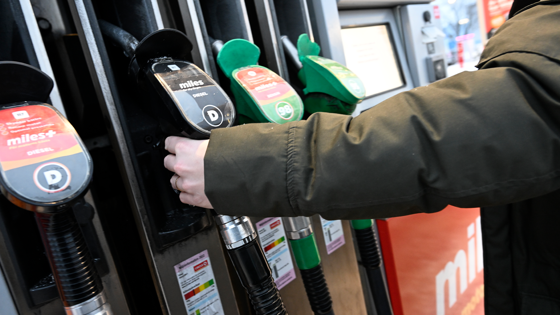 En hand som håller en grön bränsleslang vid en bensinpump.