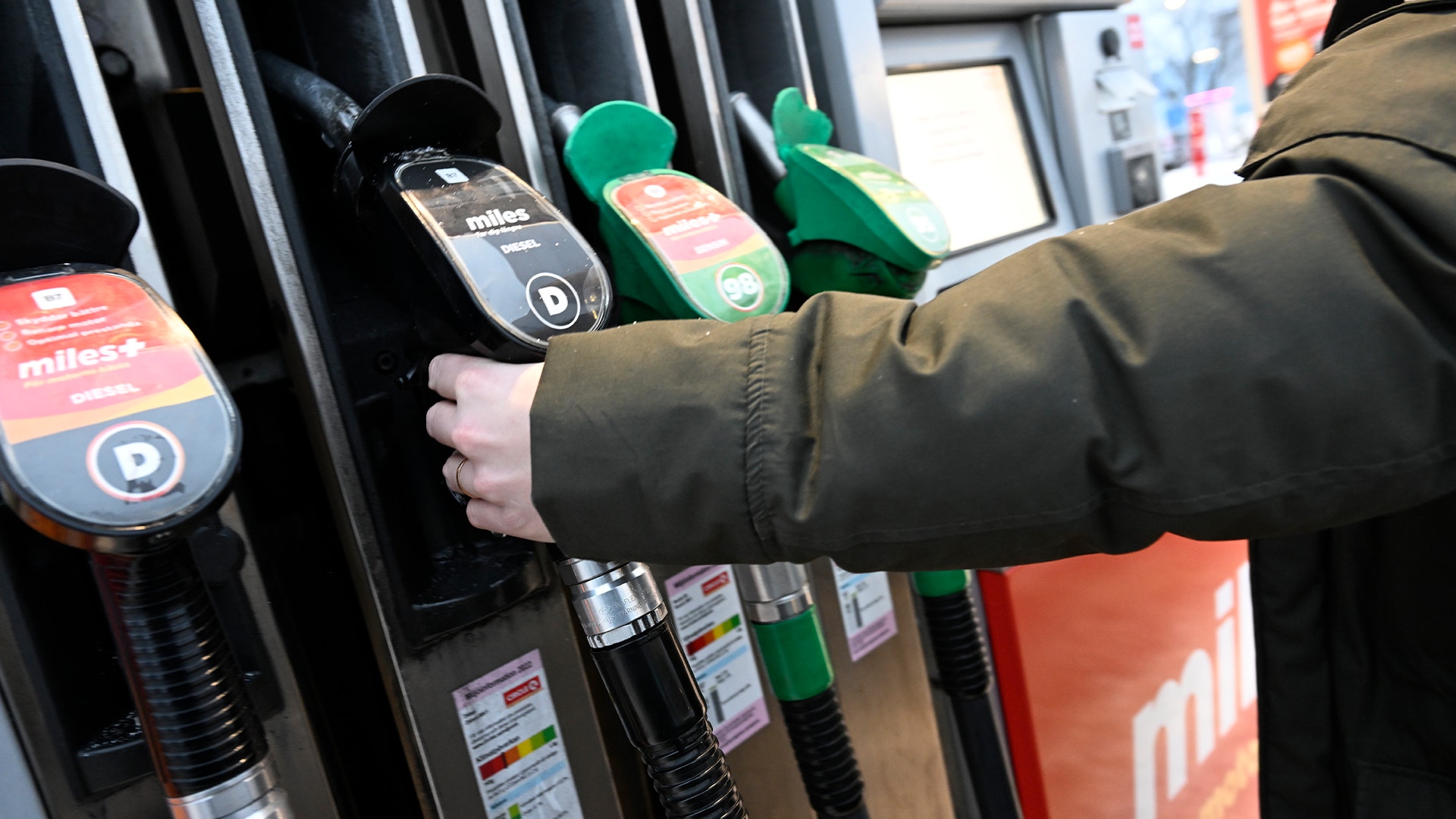 En hand som håller en grön bränsleslang vid en bensinpump.