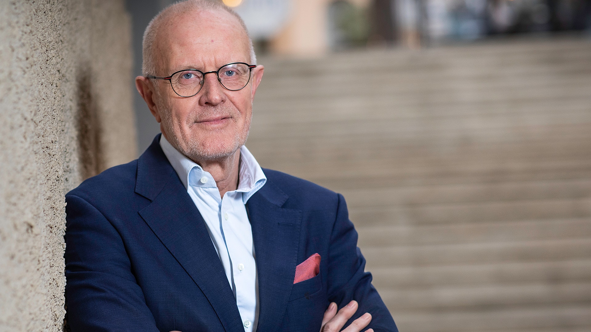 Porträtt av en man med glasögon i mörkblå kostym och vit skjorta