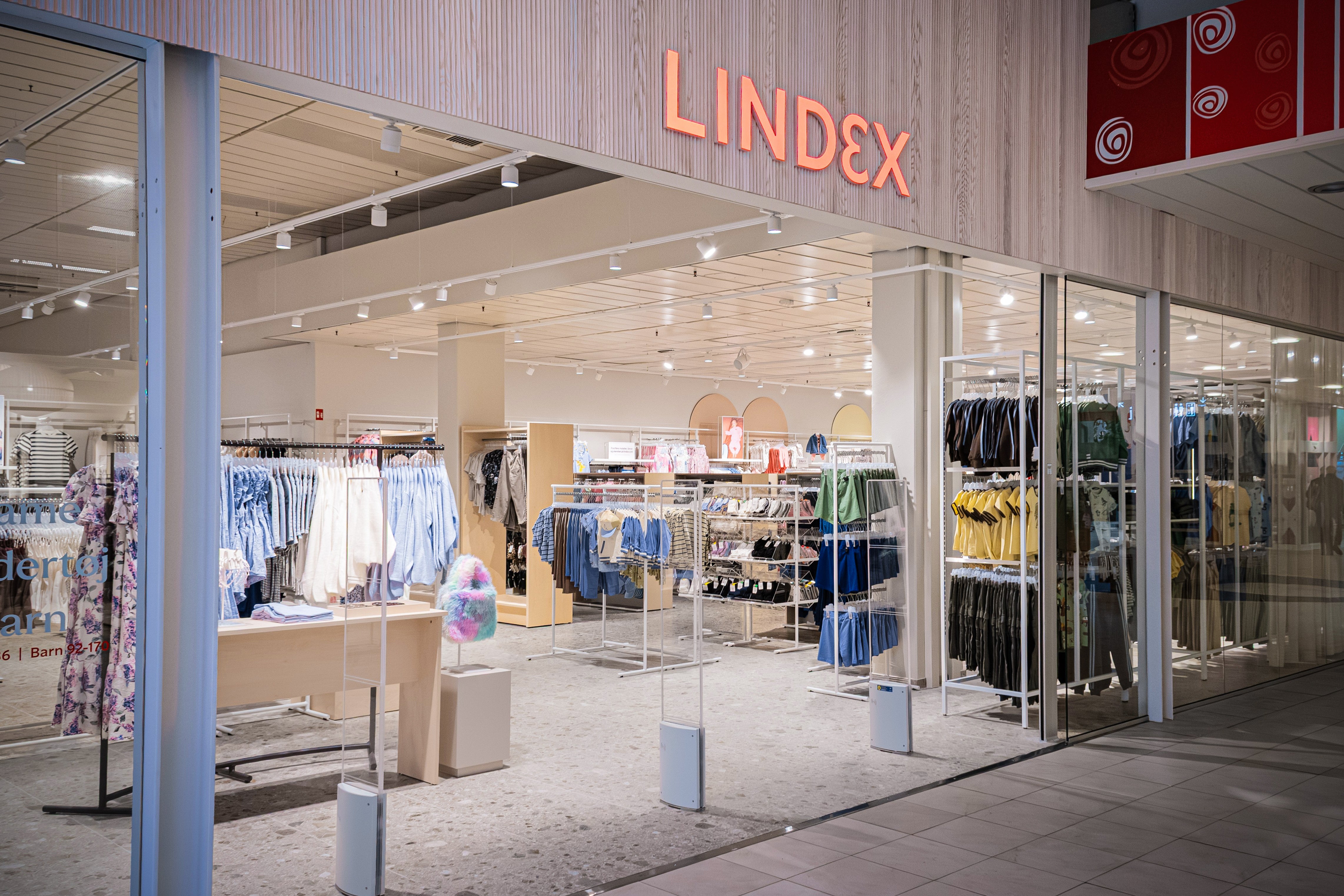 Interiör av en modern klädbutik med glasfasad och skyltfönster med kläder på displayhyllor och ställningar.