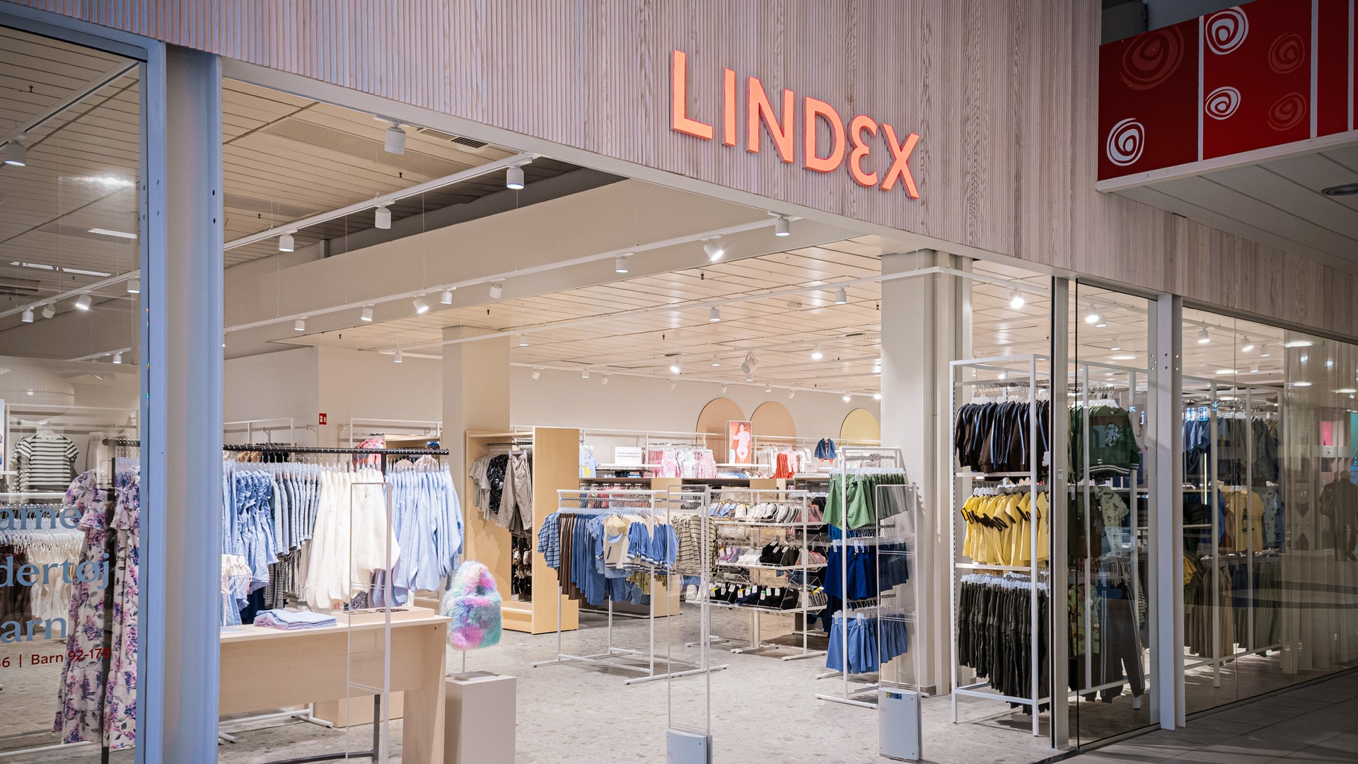 Interiör av en modern klädbutik med glasfasad och skyltfönster med kläder på displayhyllor och ställningar.