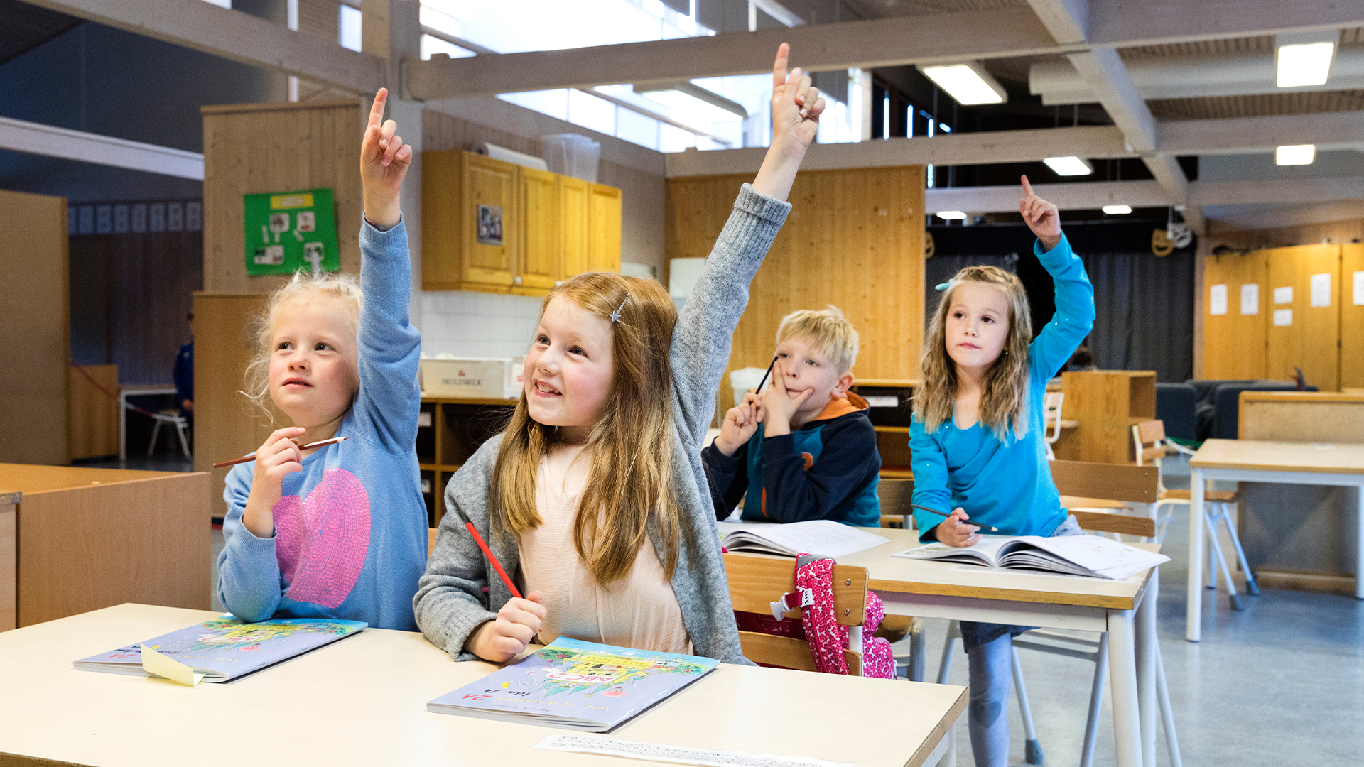 Elever i ett klassrum sitter vid bänkar och räcker upp händerna för att svara på frågor.
