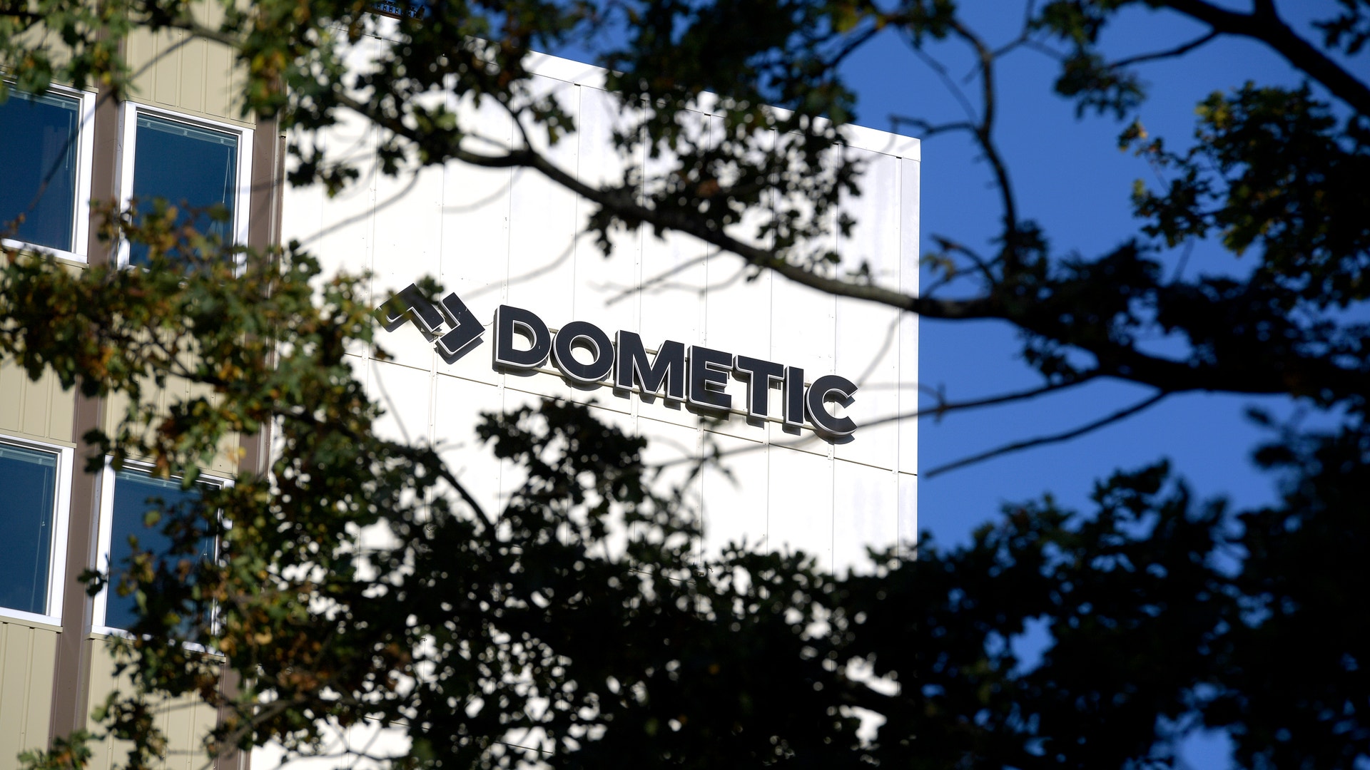 Dometics företagsbyggnad med logotyp på fasaden, omgiven av träd.