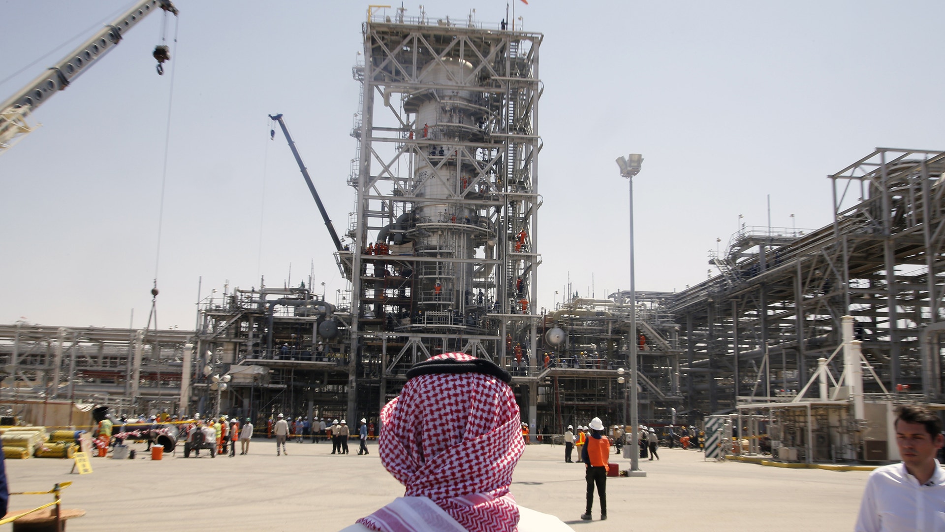 En person i traditionell arabisk huvudduk står framför en stor industrianläggning med torn, kranar och metallkonstruktioner under konstruktion.