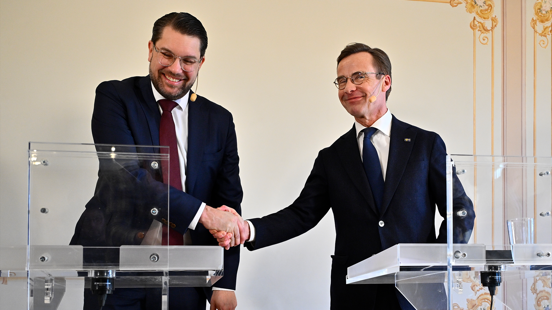 Två män i mörka kostymer skakar hand vid ett officiellt möte.