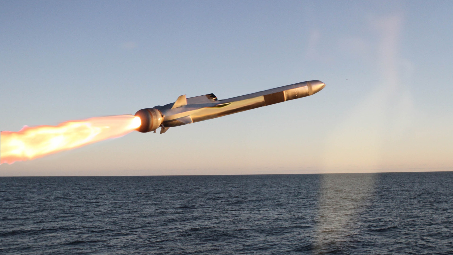 En missil avfyras över havet med flammande raket och klar himmel i bakgrunden.