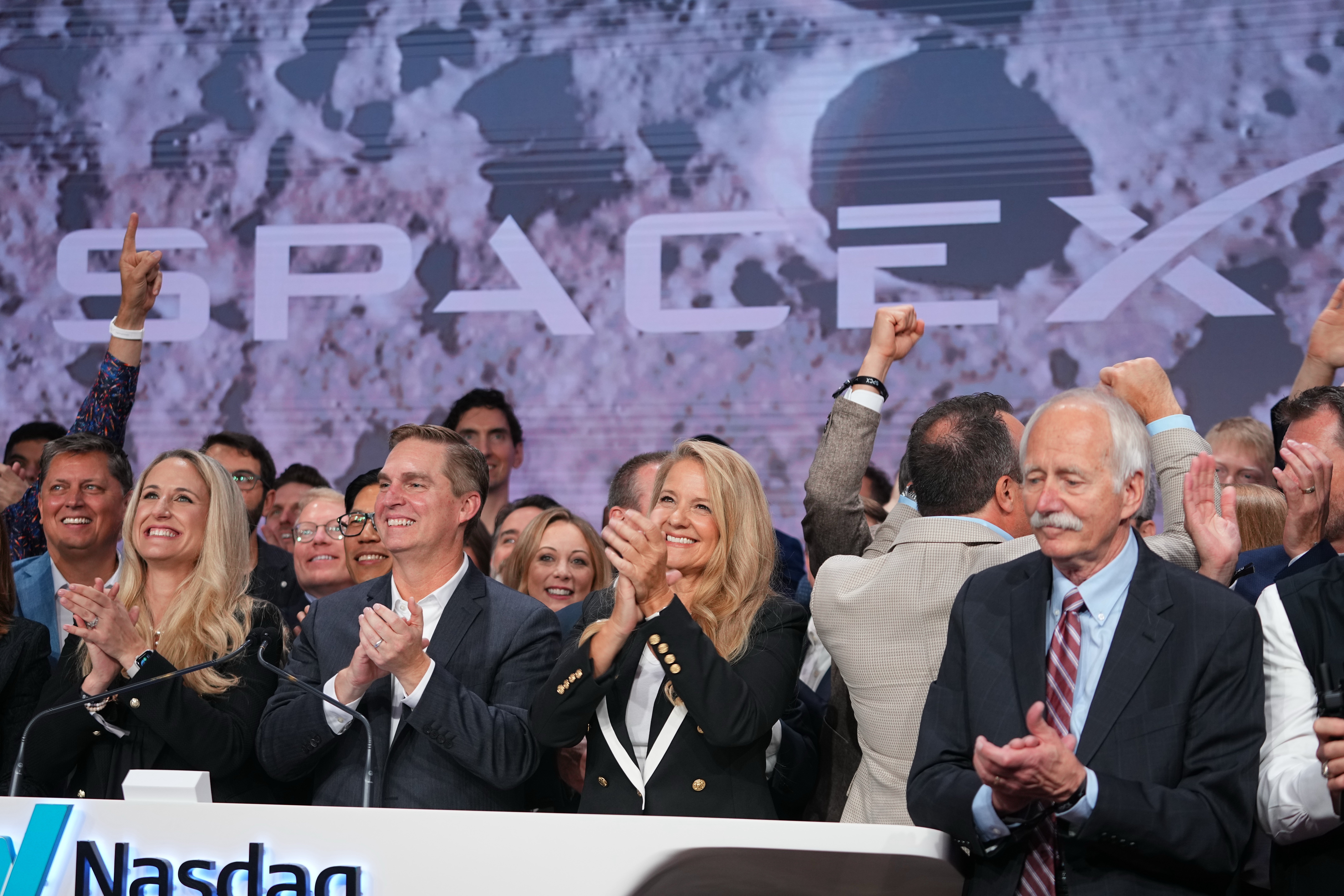 En grupp människor i affärskläder firar tillsammans på Nasdaq-börsen med upphöjda händer och glada miner.