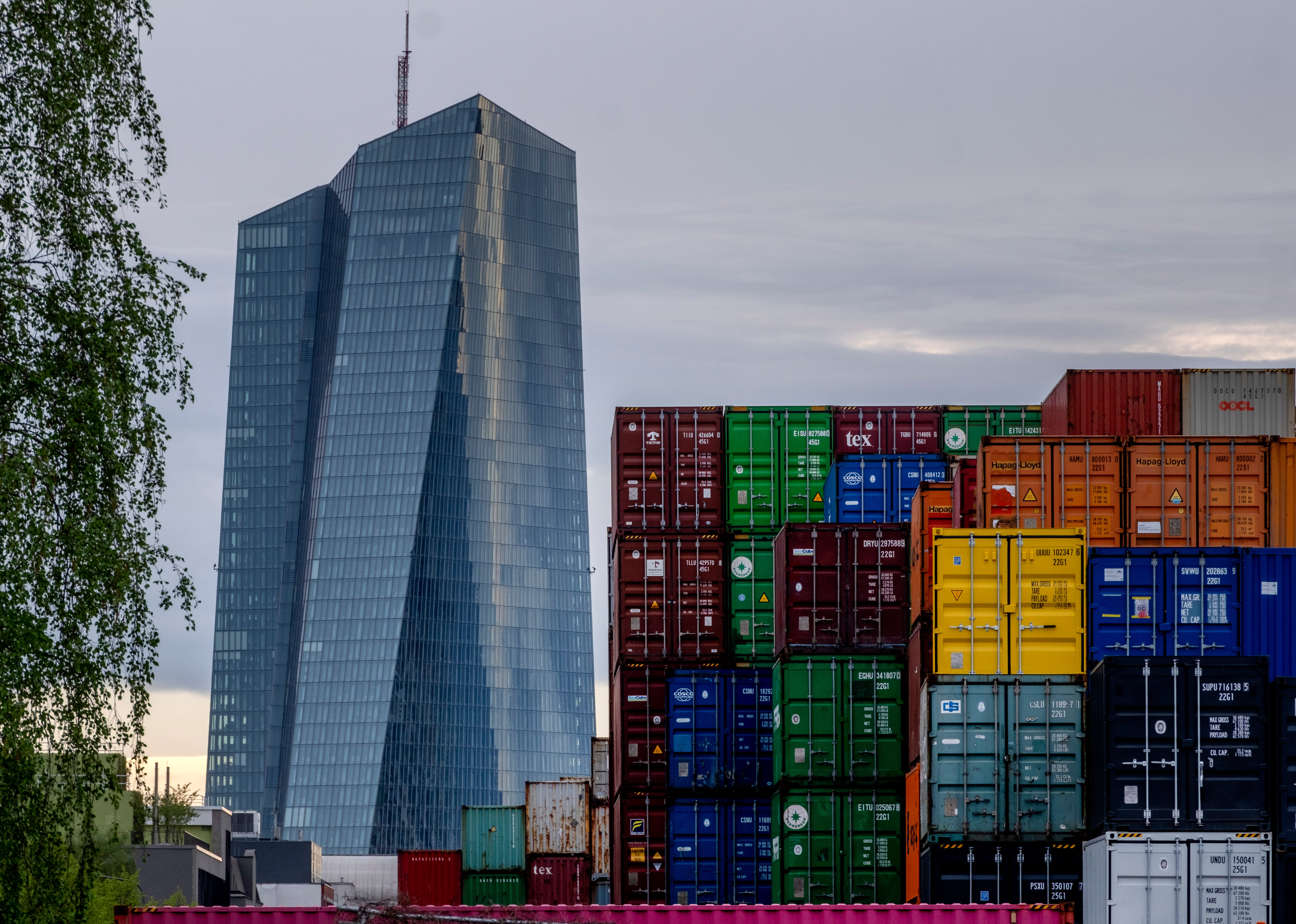 Europeiska centralbankens glasskyskrapa i Frankfurt bakom höga staplar av färgglada fraktcontainrar.