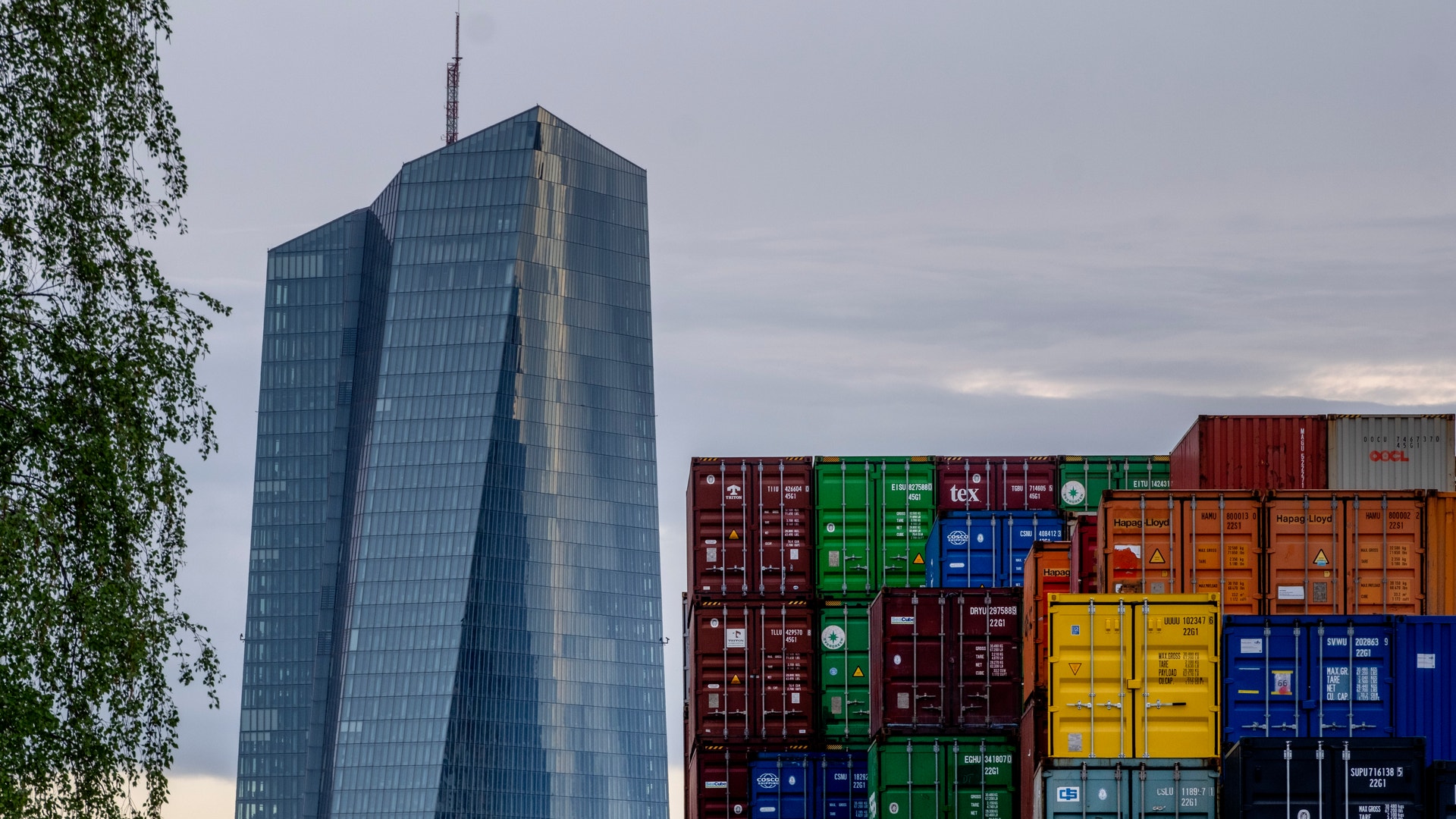 Europeiska centralbankens glasskyskrapa i Frankfurt bakom höga staplar av färgglada fraktcontainrar.