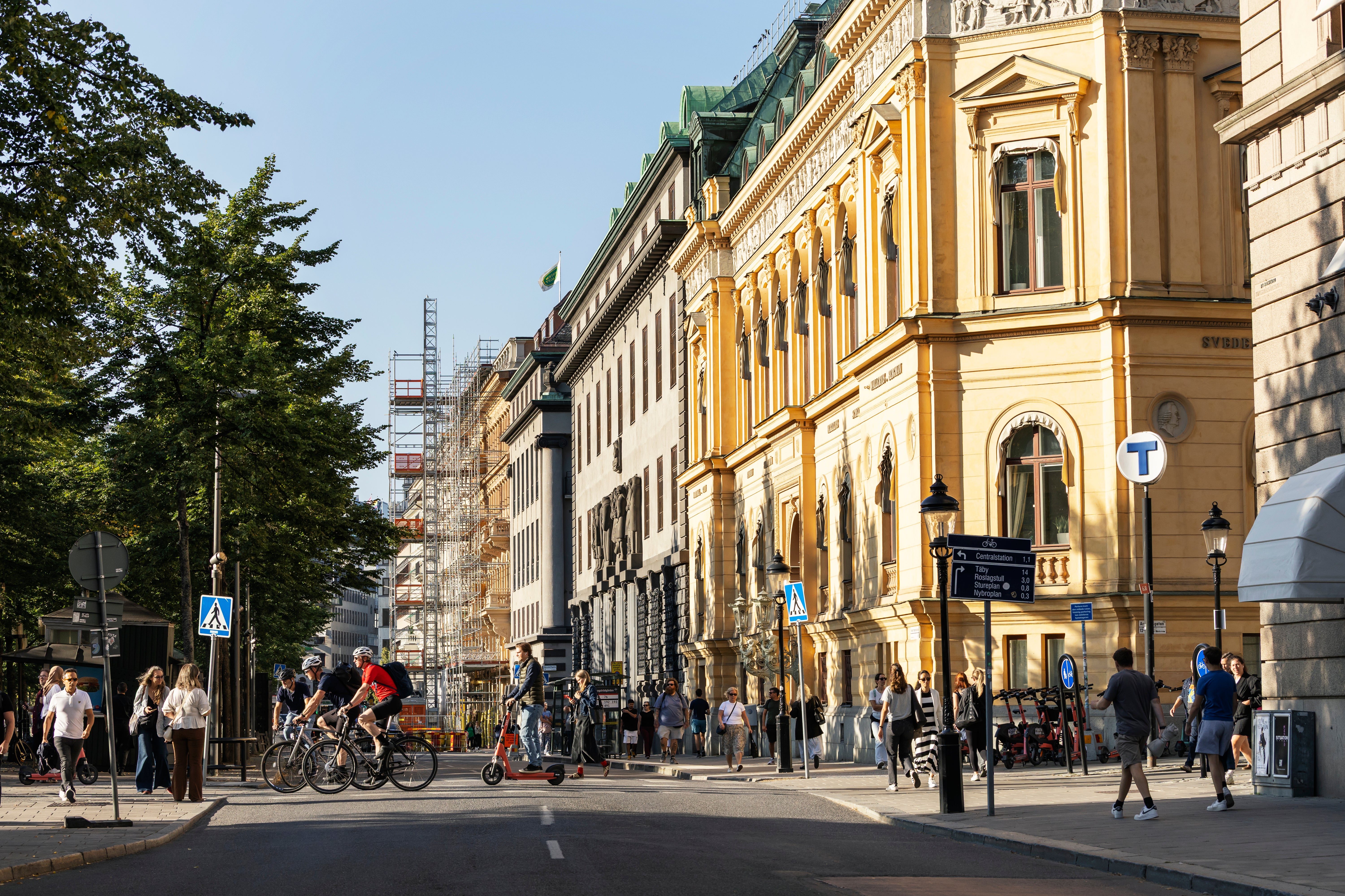 En stadsgata med klassiska gula byggnader, människor som går och cyklar, och blå himmel.