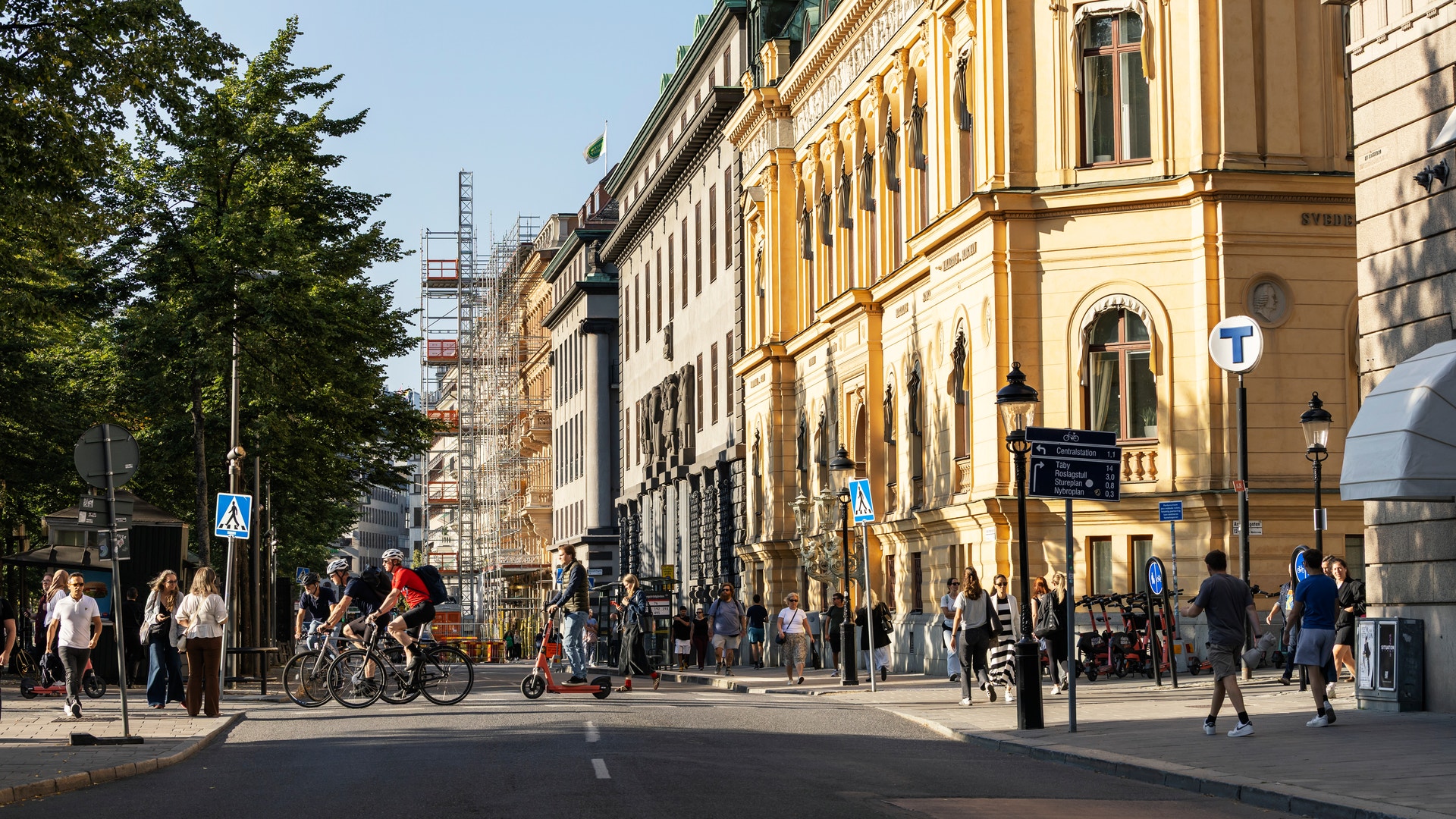 En stadsgata med klassiska gula byggnader, människor som går och cyklar, och blå himmel.