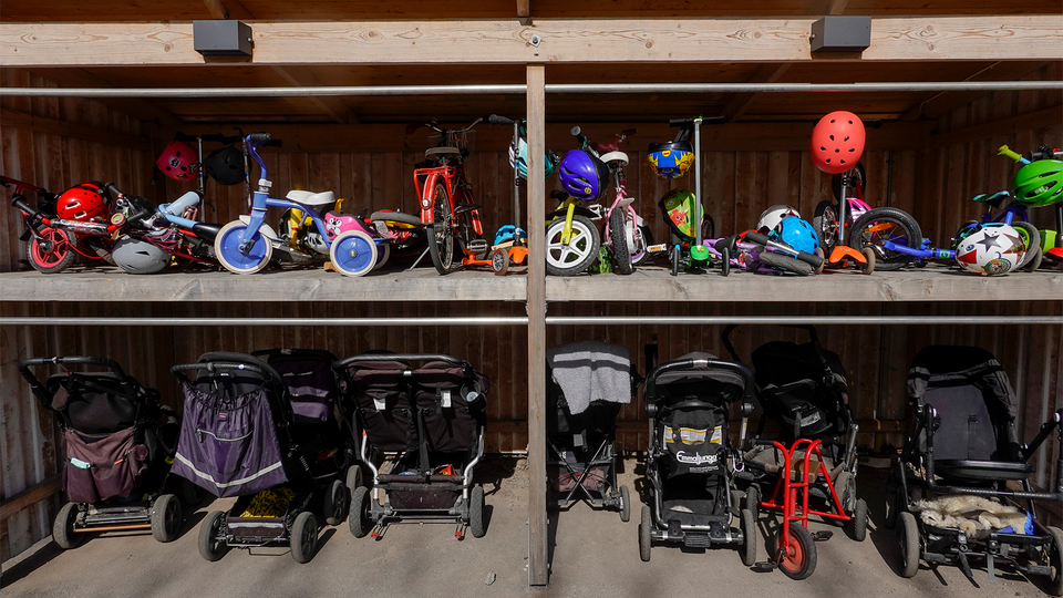 Sparkcyklar, barnvagnar och små cyklar vid en barnvagnsparkering utanför en förskola.