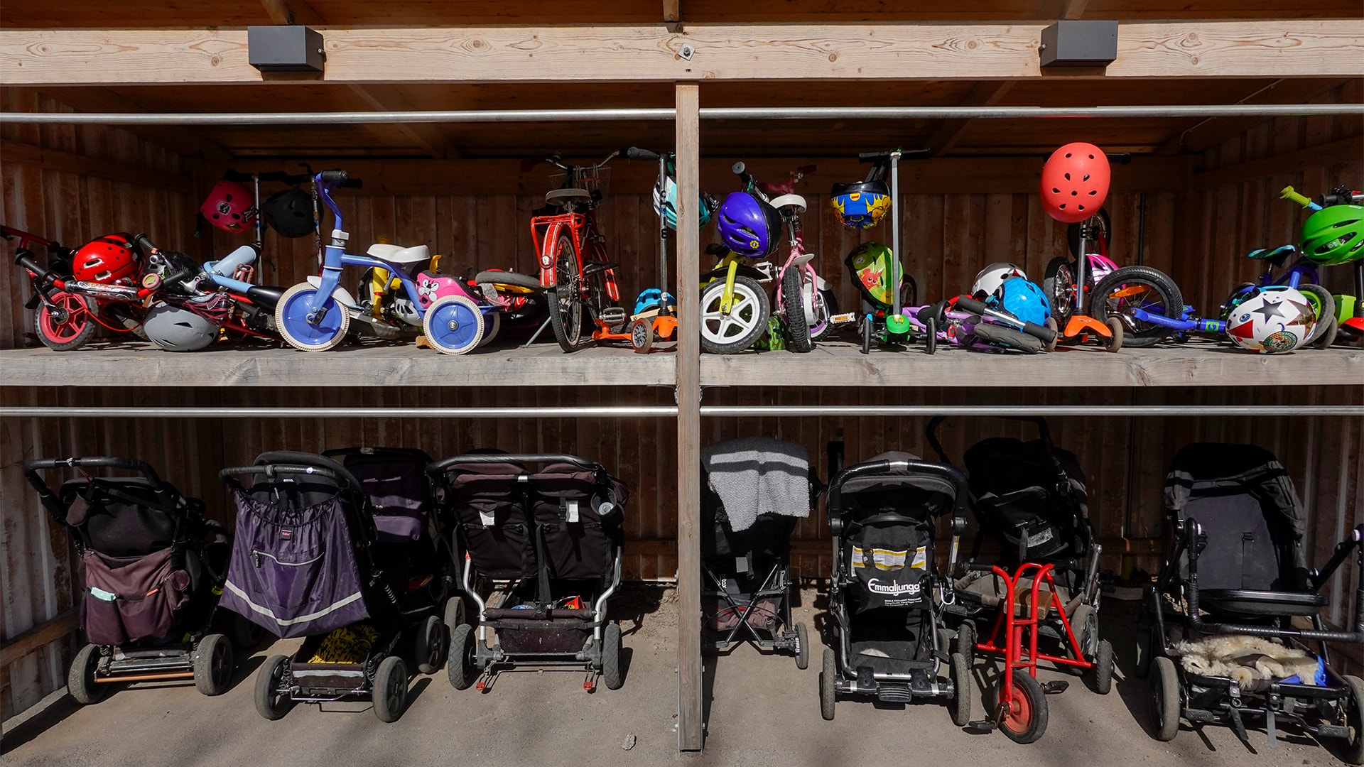 Sparkcyklar, barnvagnar och små cyklar vid en barnvagnsparkering utanför en förskola.