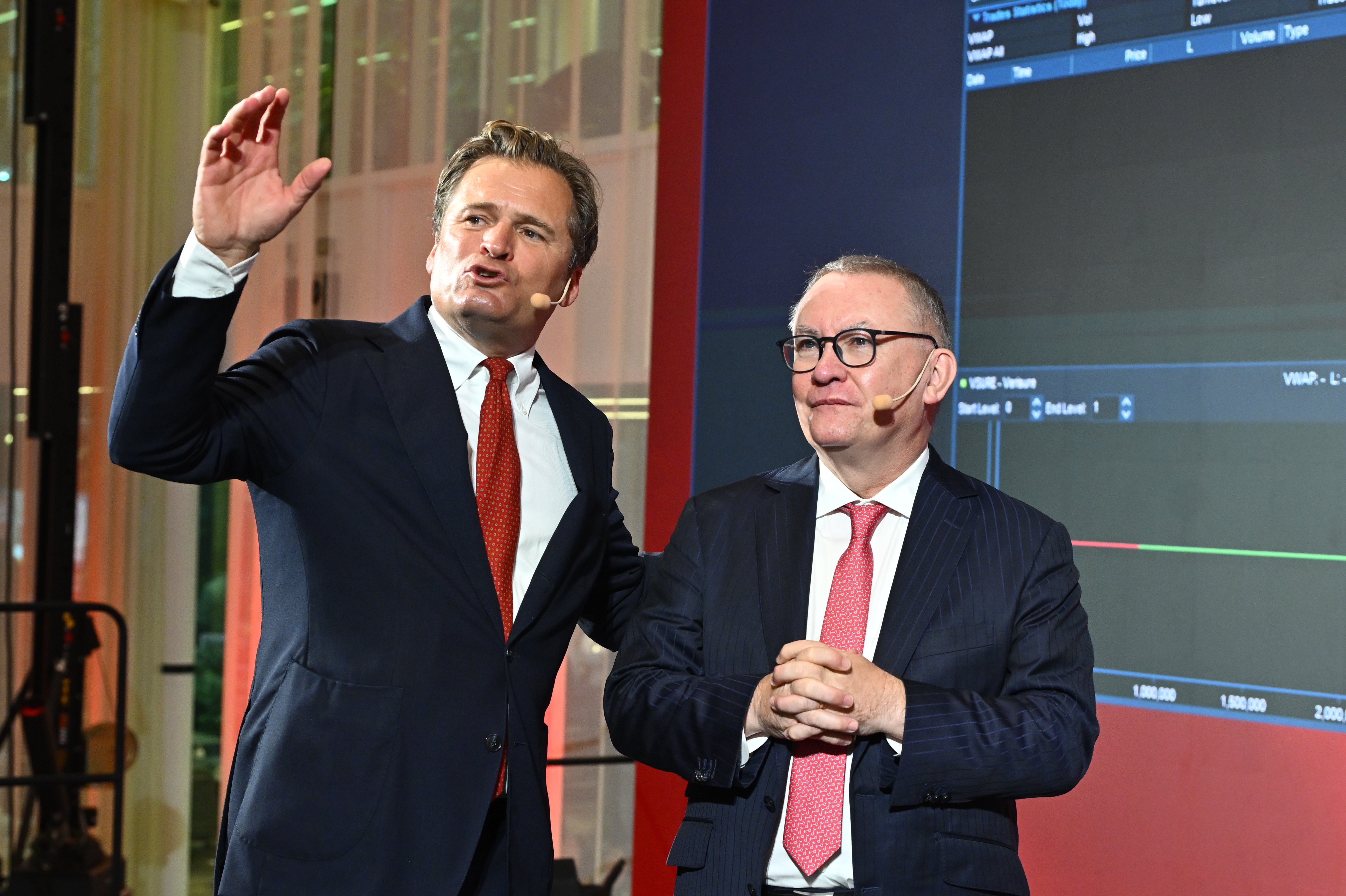 Två män i kostym presenterar på en scen framför en skärm