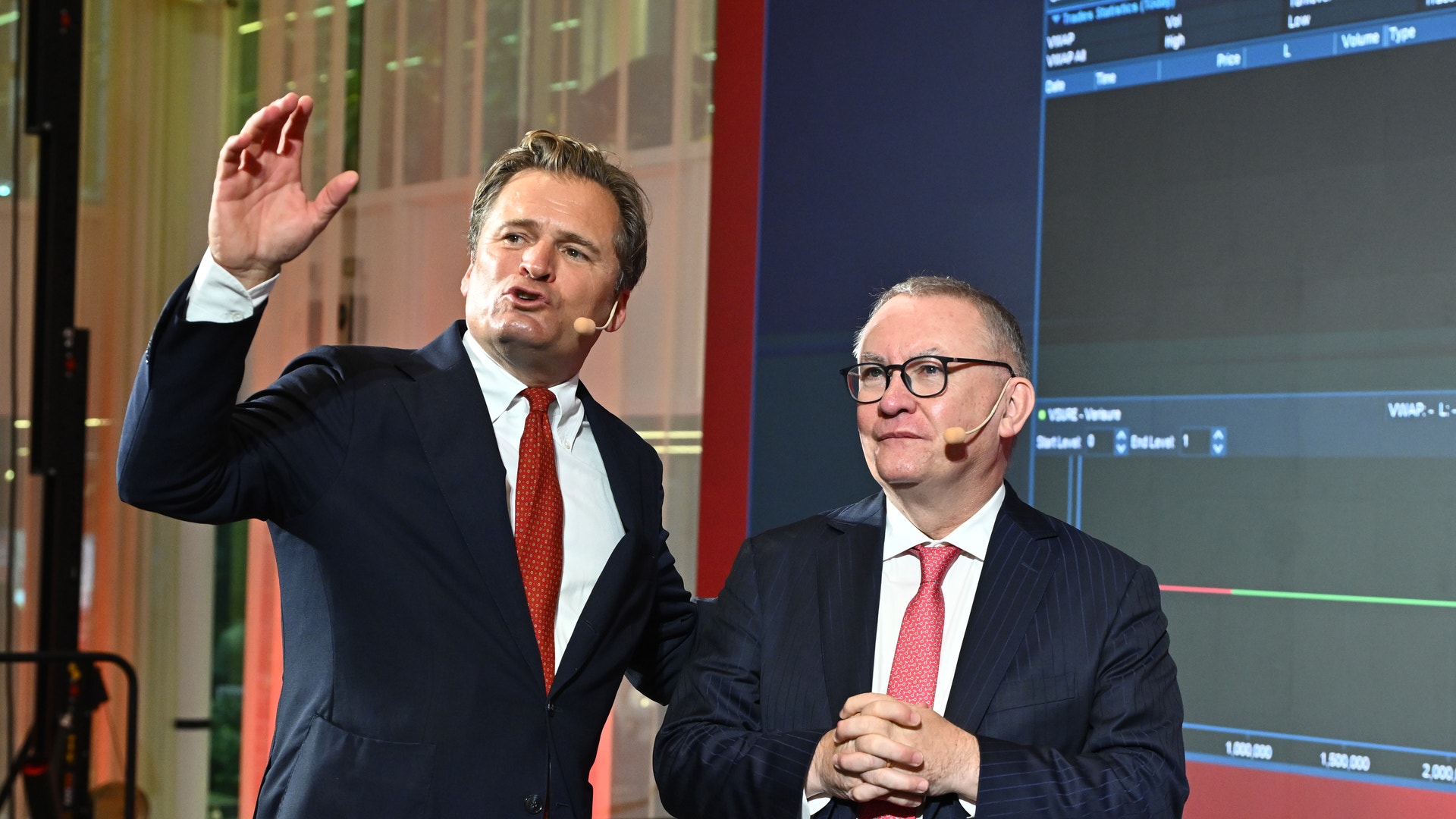 Två män i kostym presenterar på en scen framför en skärm