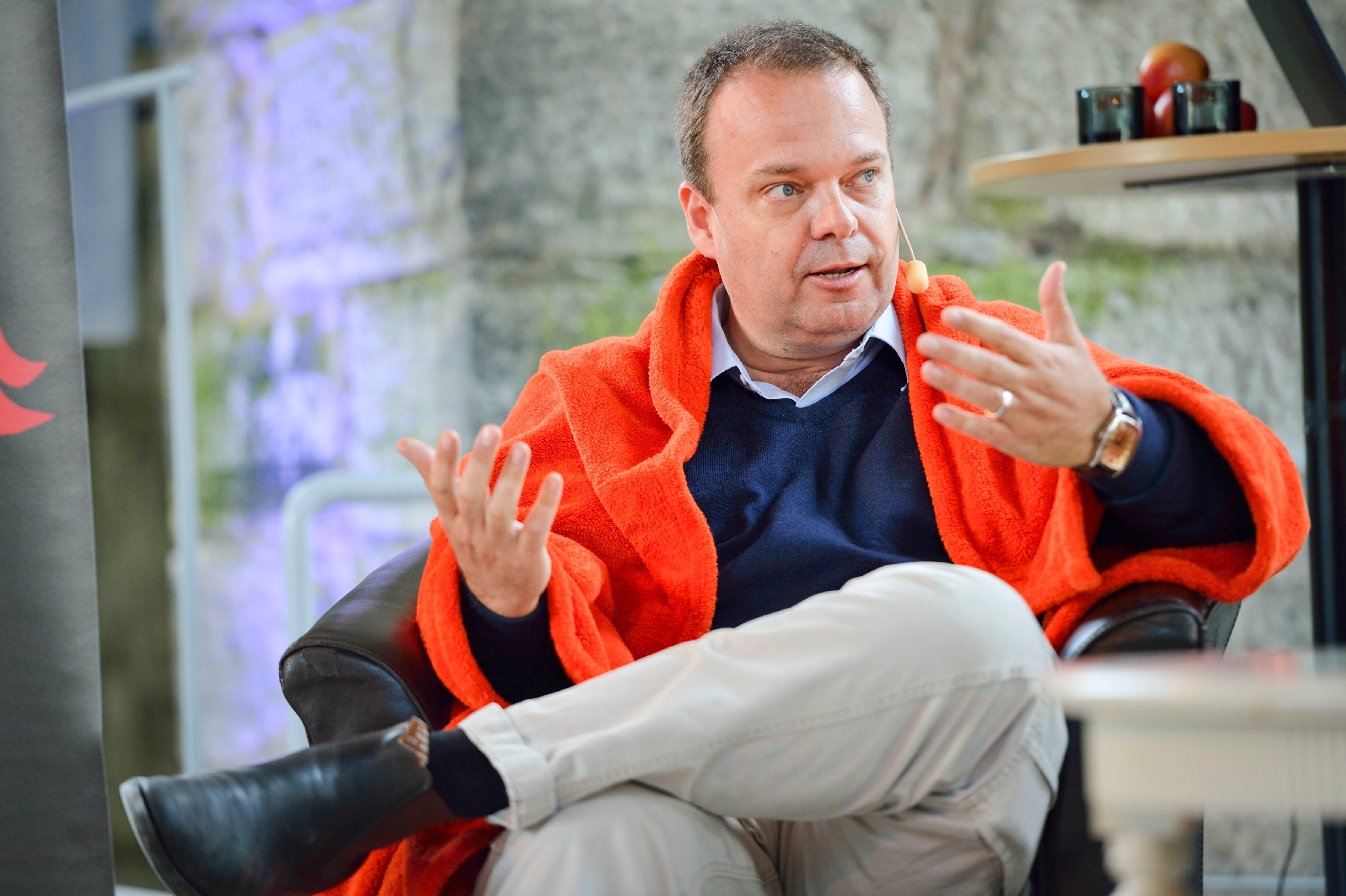 Sven Otto Littorin i orange jacka sitter och gestikulerar medan han talar.