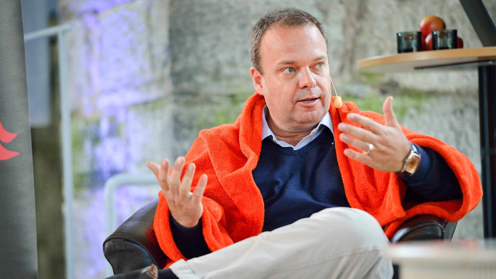 Sven Otto Littorin i orange jacka sitter och gestikulerar medan han talar.