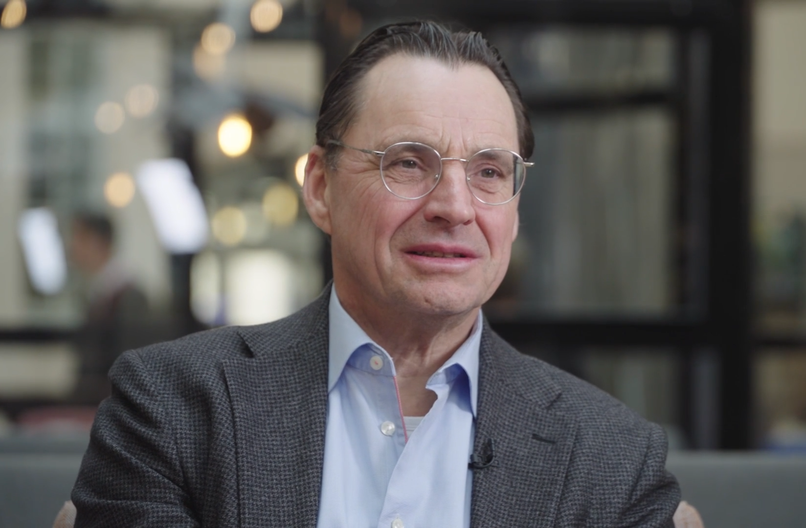 Porträtt av en man med glasögon och grå blazer framför en suddig bakgrund.