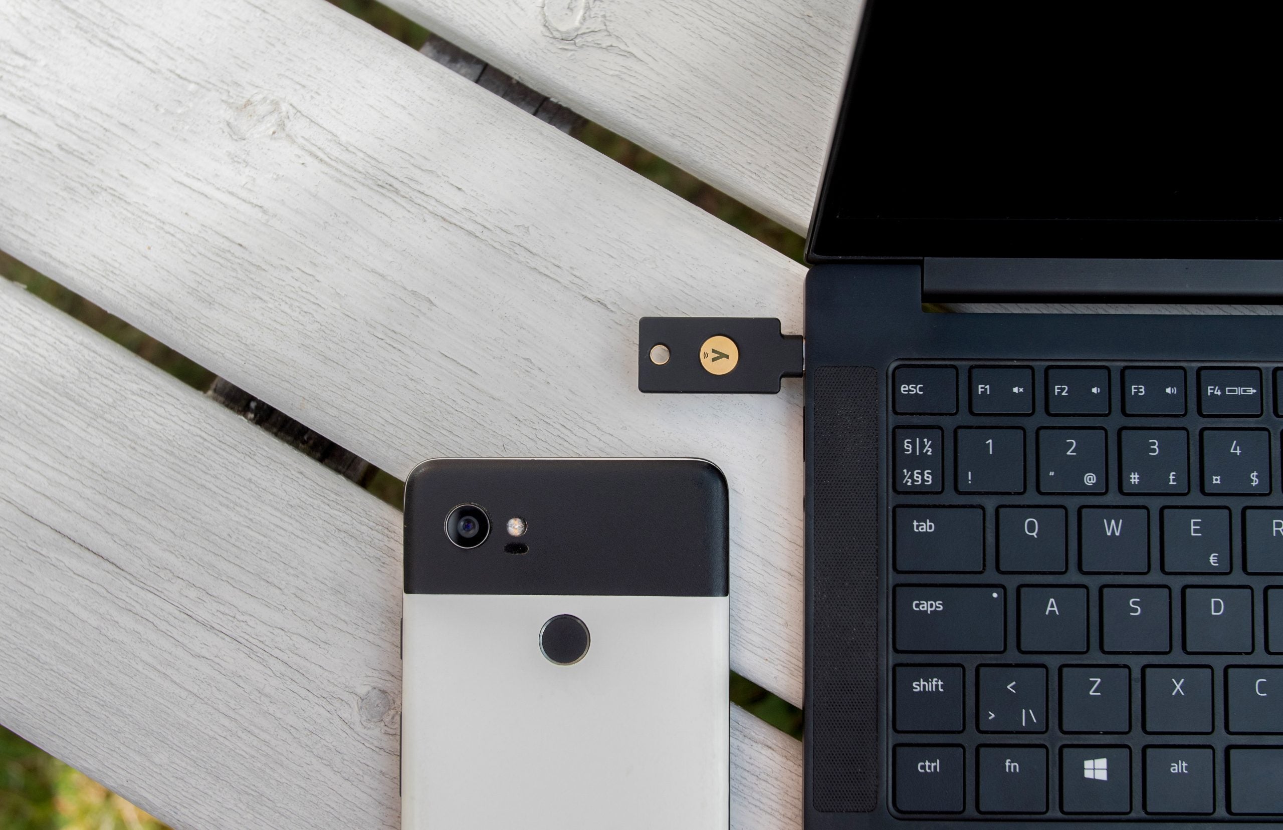 En smartphone, en laptopkomputer och ett USB-dongle ligger på en ljus träyta, vilket visar en modern arbetsplats.