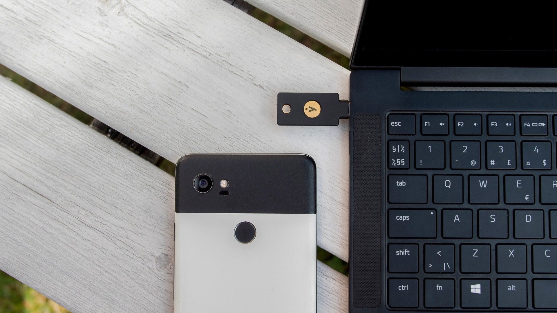 En smartphone, en laptopkomputer och ett USB-dongle ligger på en ljus träyta, vilket visar en modern arbetsplats.
