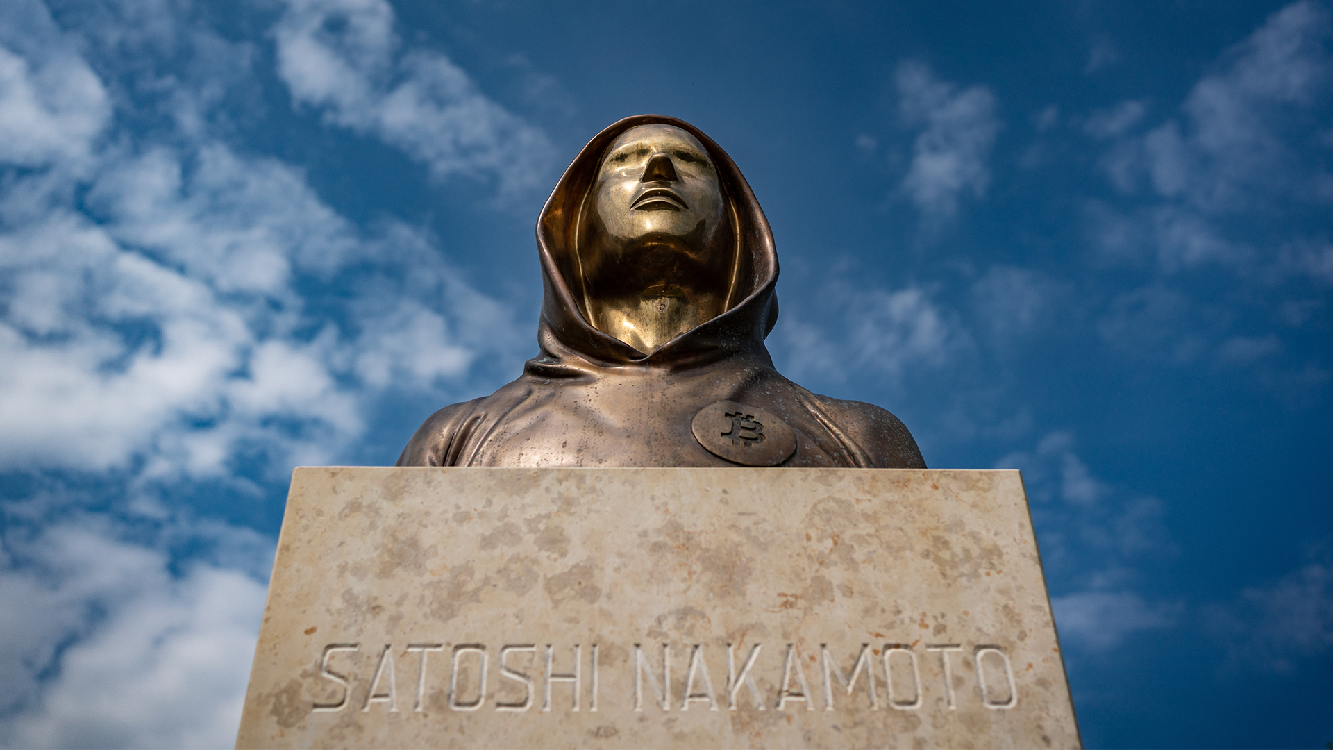 Bronsstaty av Satoshi Nakamoto mot blå himmel med vita moln