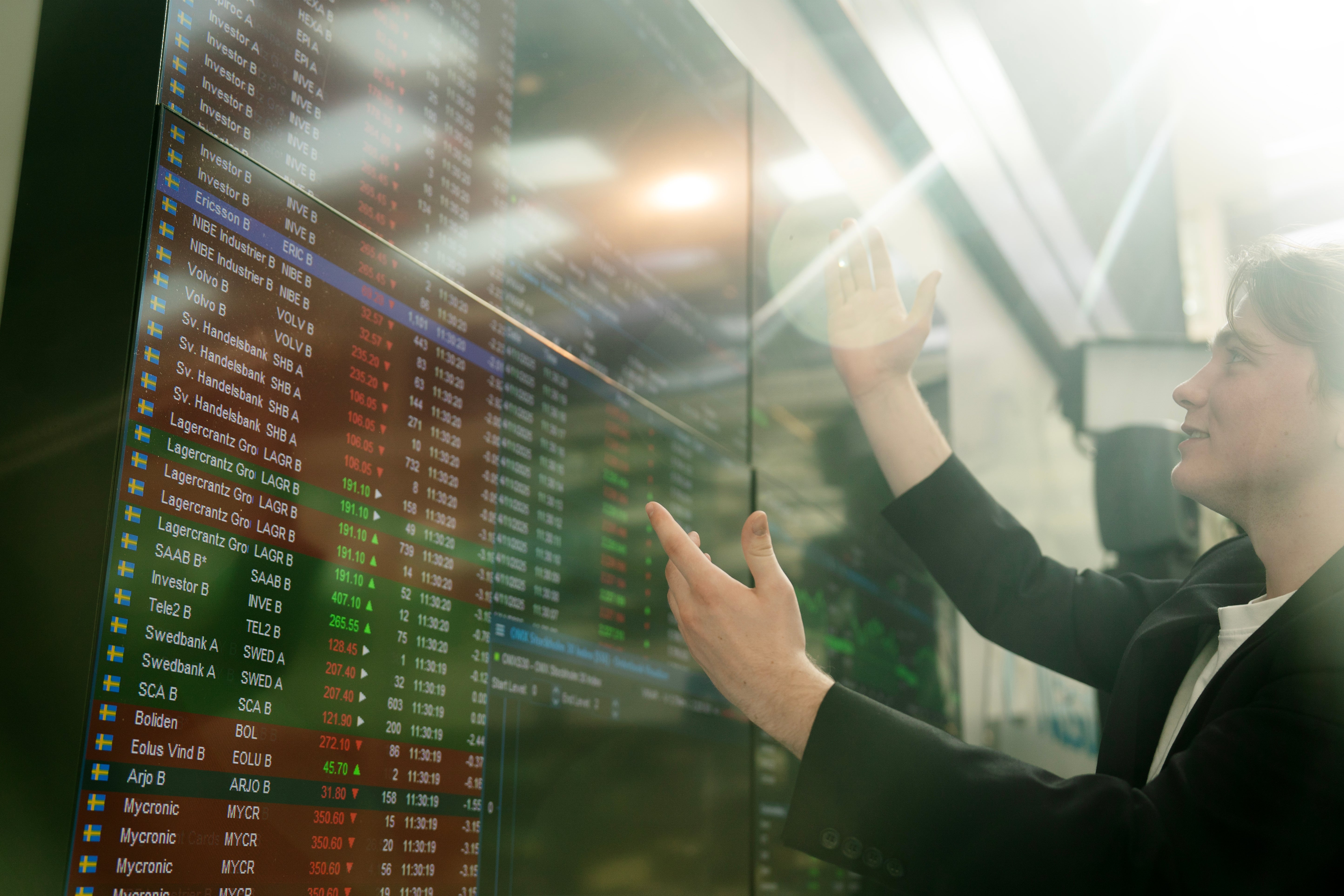 Person som pekar på en aktiemarknadsskärm med finansiell data och börskurser