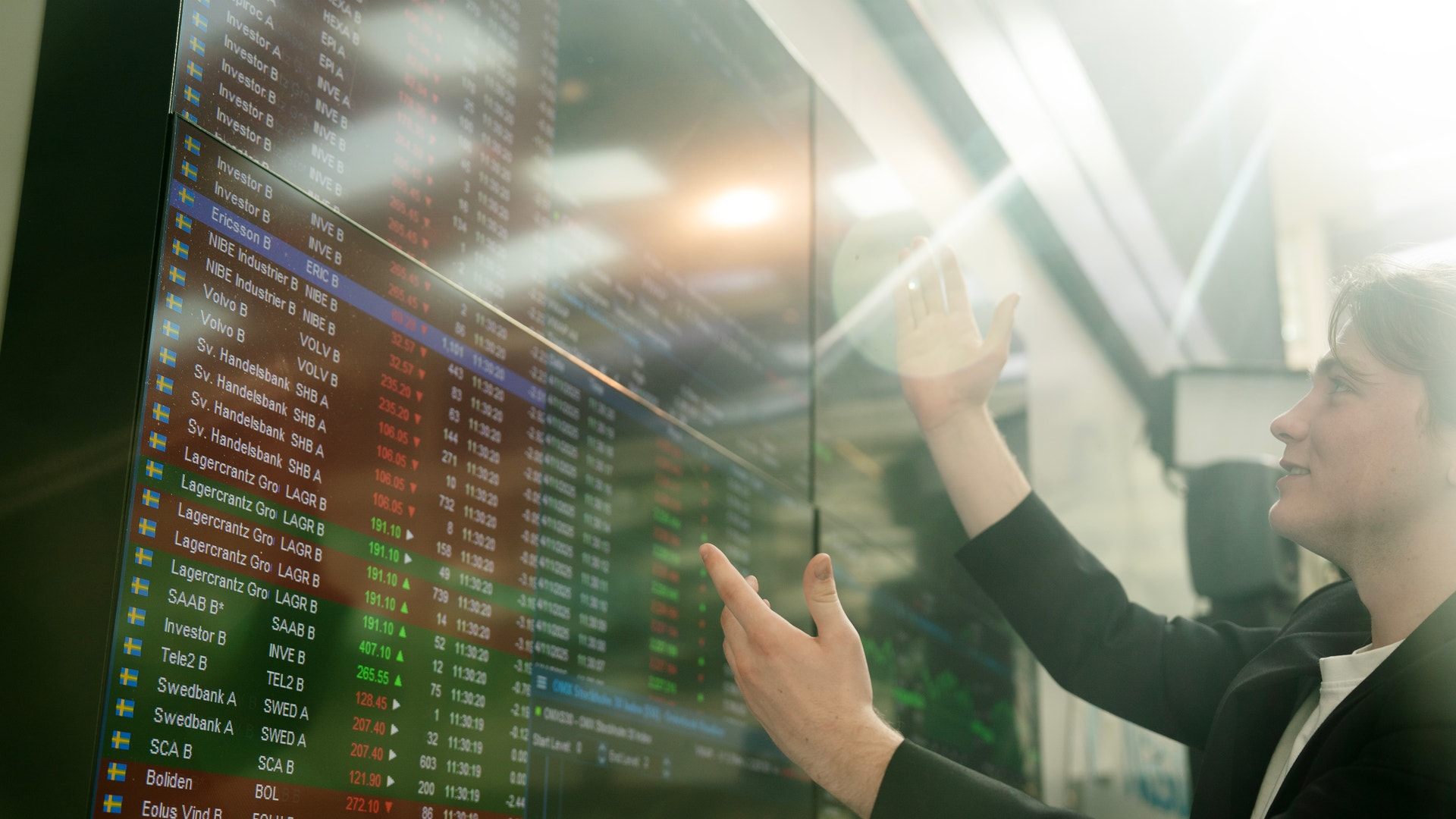 Person som pekar på en aktiemarknadsskärm med finansiell data och börskurser