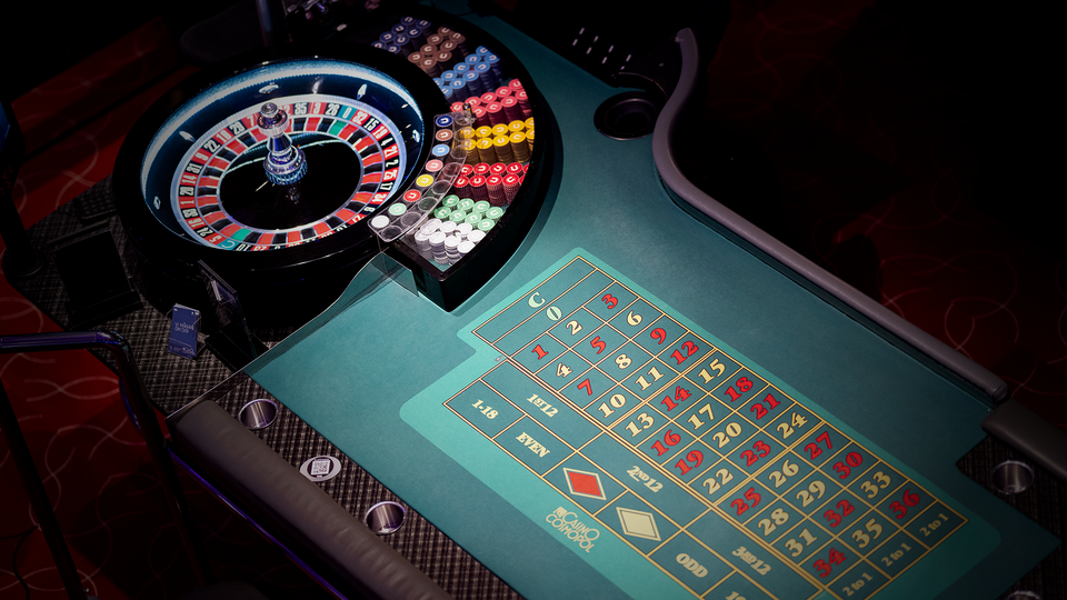 Livecasino-bord med ett klassiskt rouletthjul med röda och svarta nummer, samt ett grönt spelplan framför det. Hjulet är belyst med färgglada LED-lampor i blått, rött och gult. Spelplanen visar olika spelalternativ med nummer och symboler för betting.