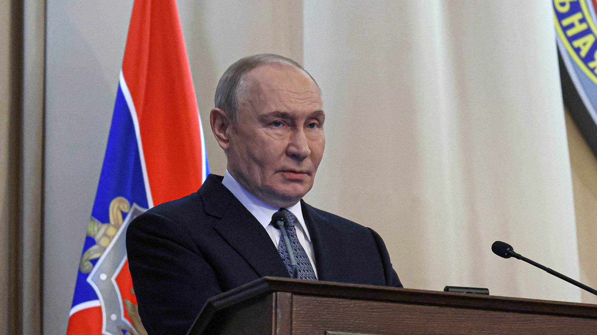 Man i kostym vid podium med rysk flagga i bakgrunden