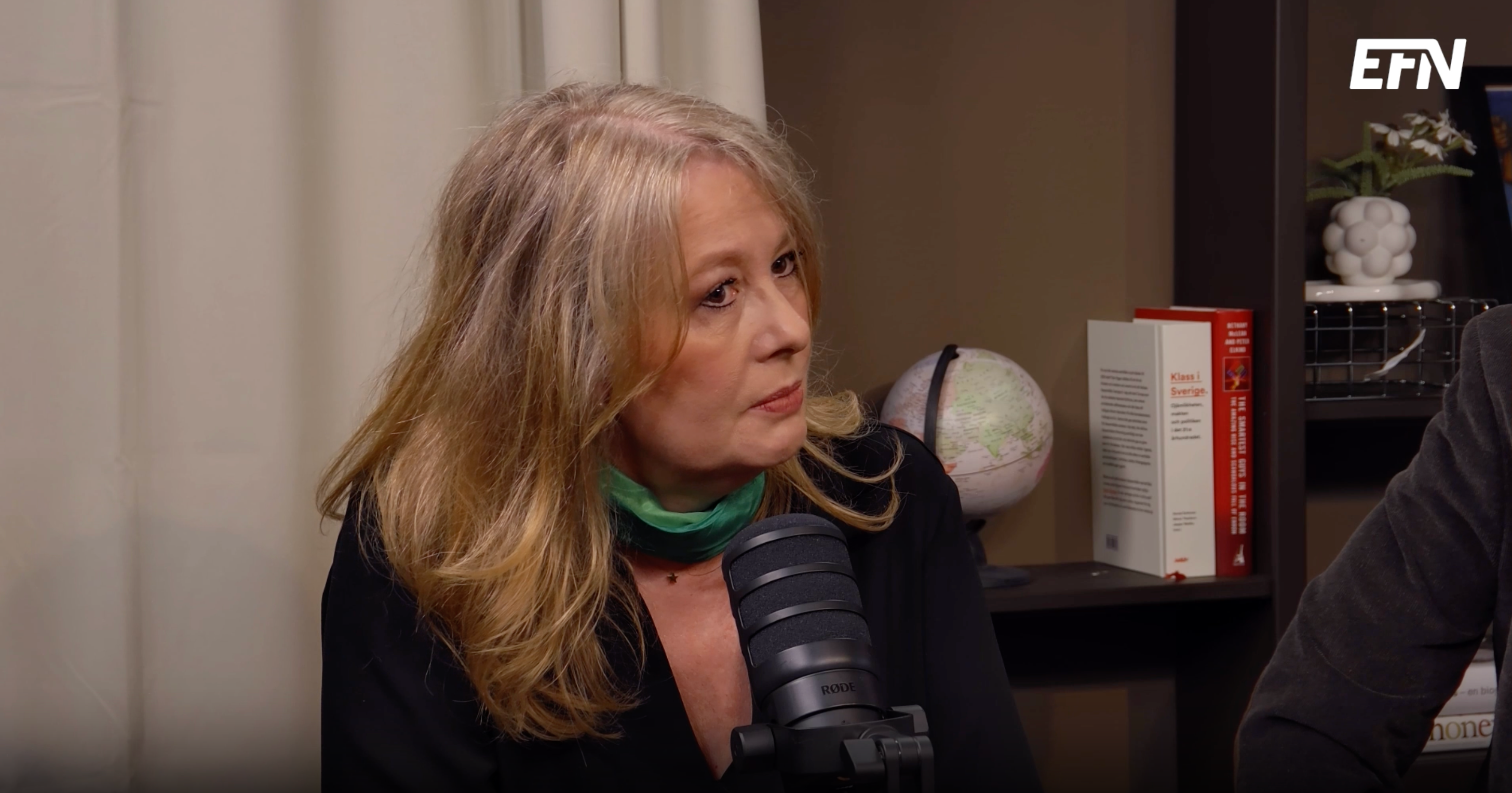 En kvinna med långt blont hår pratar in i en mikrofon under en podcastinspelning.