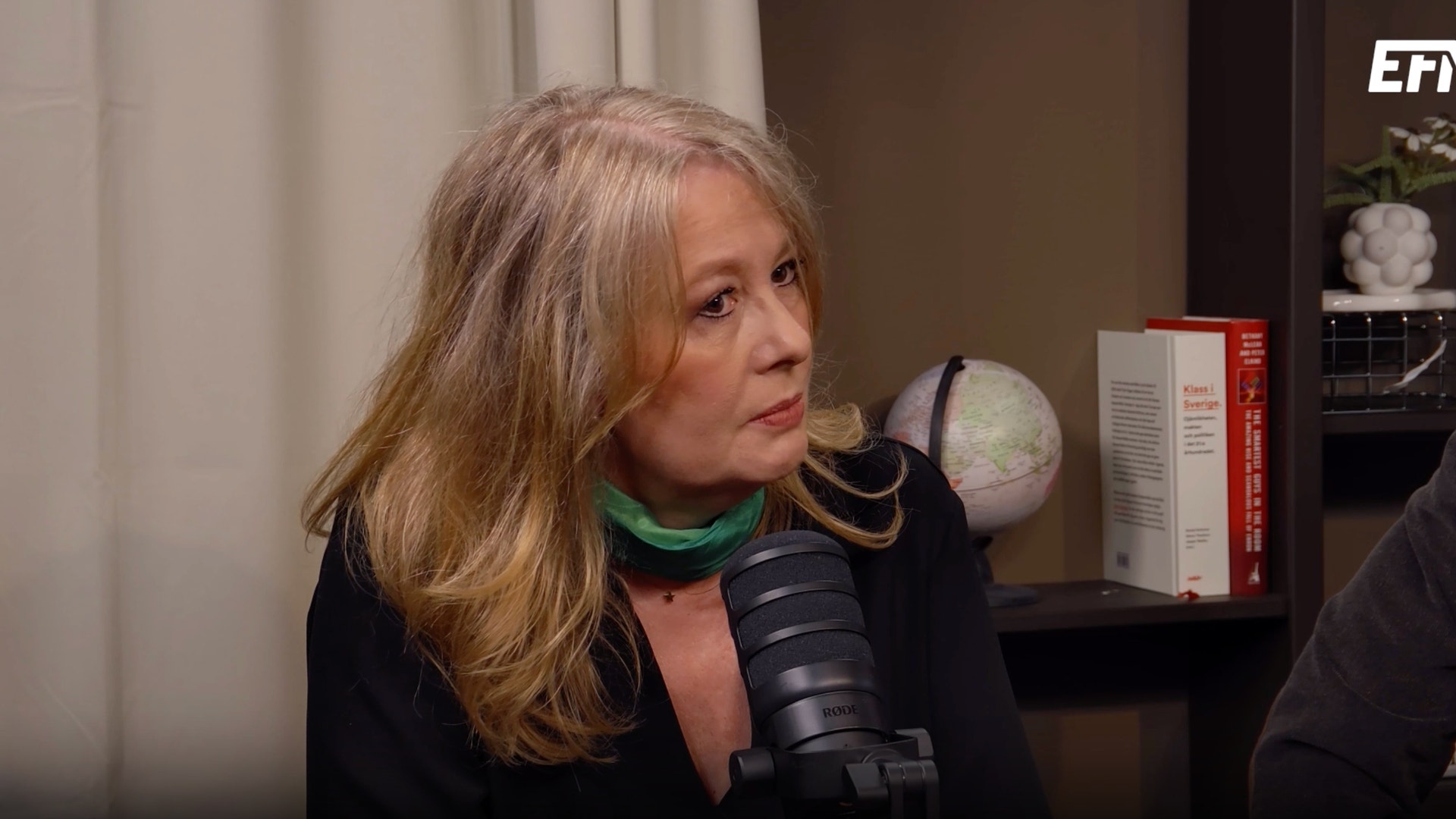 En kvinna med långt blont hår pratar in i en mikrofon under en podcastinspelning.
