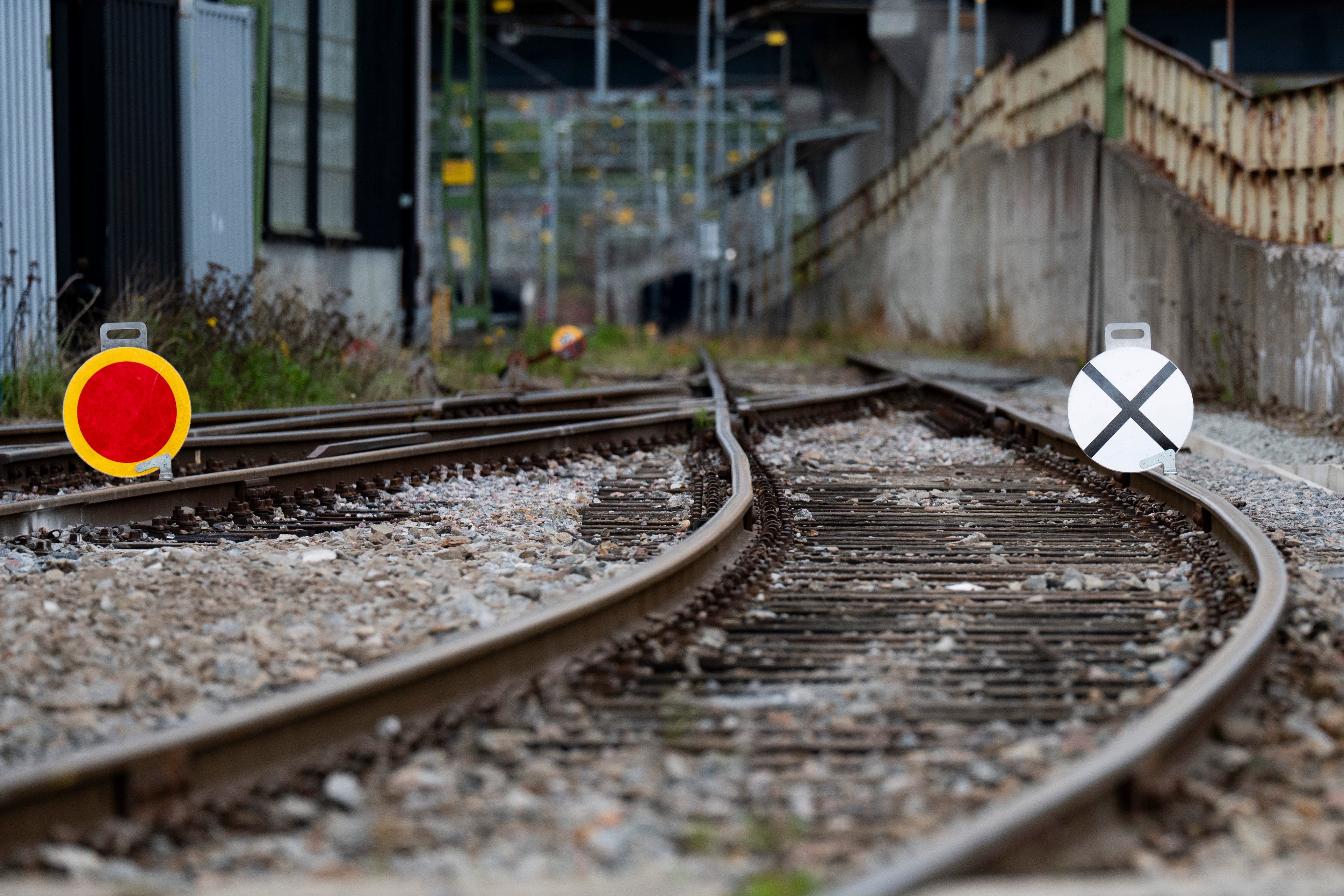 Två järnvägsspår som korsar varandra. Det vänstra spåret är markerat med en röd och gul cirkel, det högra med ett vitt kryss. Urbana byggnader syns i bakgrunden.