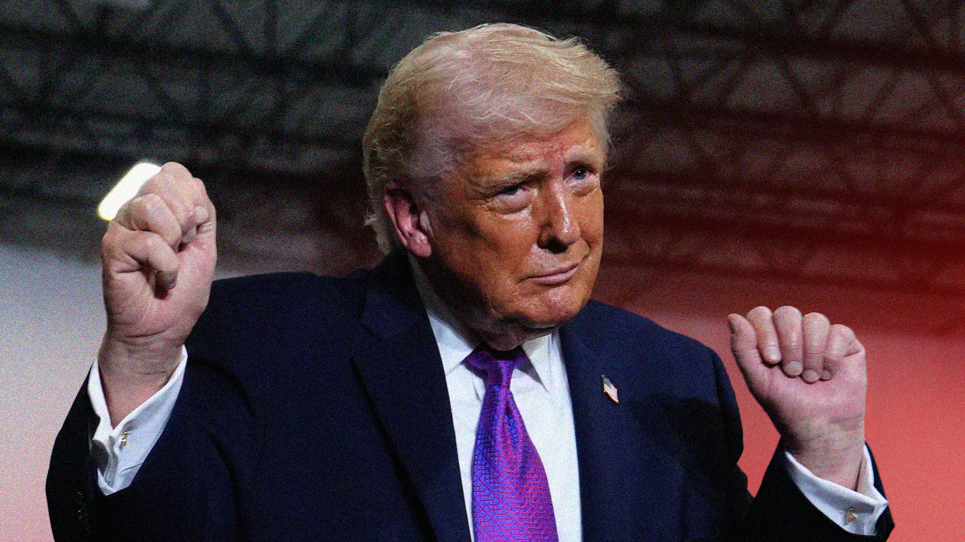 Man i mörk kostym och lila slips med båda närvarna upphöjda i en triumfande gest