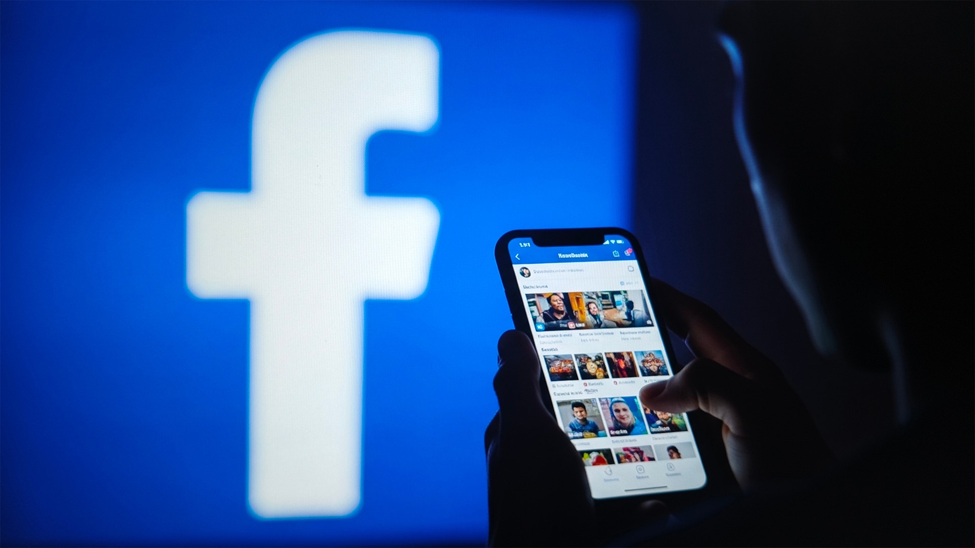 Facebooks logotyp på blå bakgrund med en hand som håller en smartphone som visar Facebooks mobilapp.