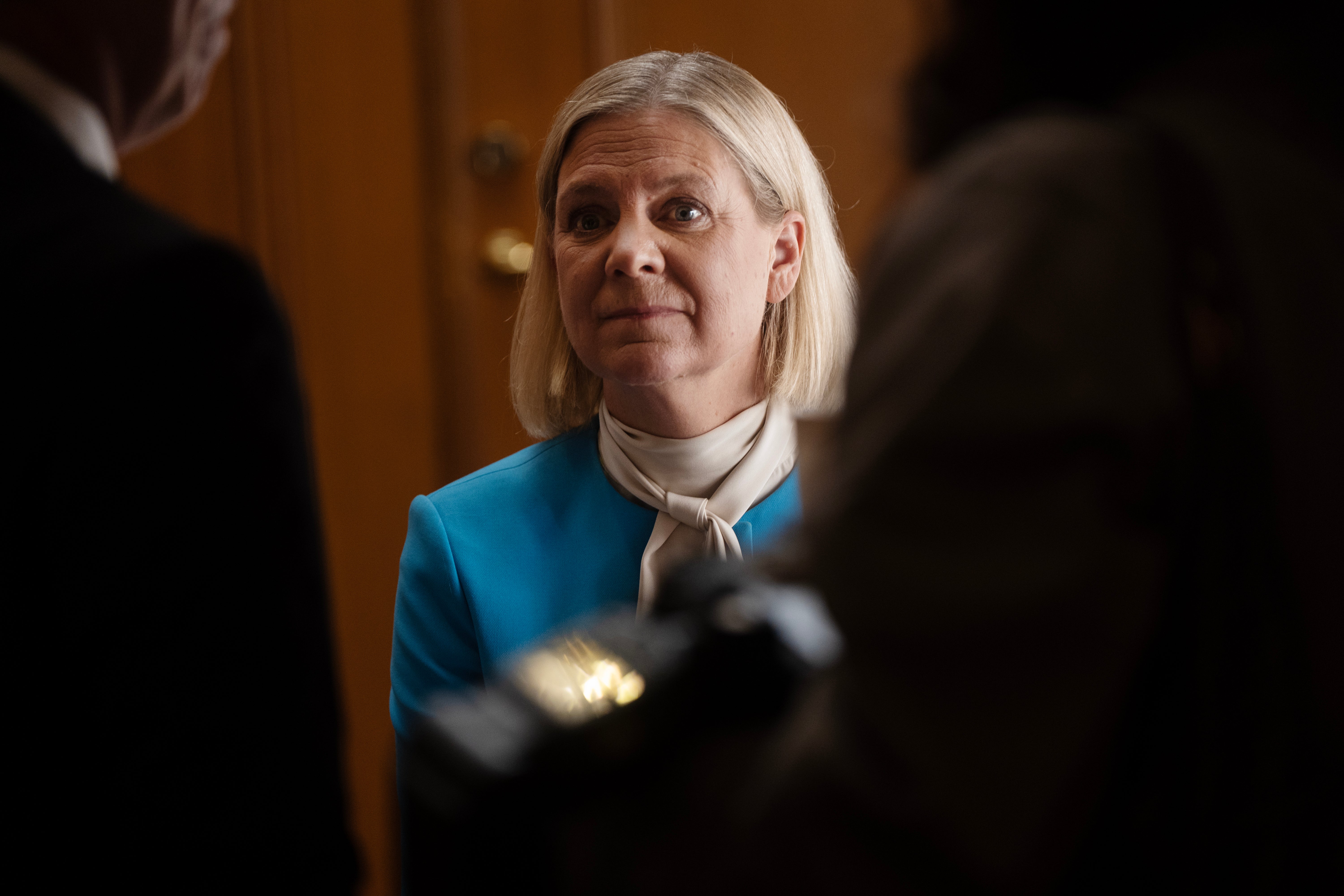 En kvinna i blå kavaj och sjal omgiven av personer i en korridor.