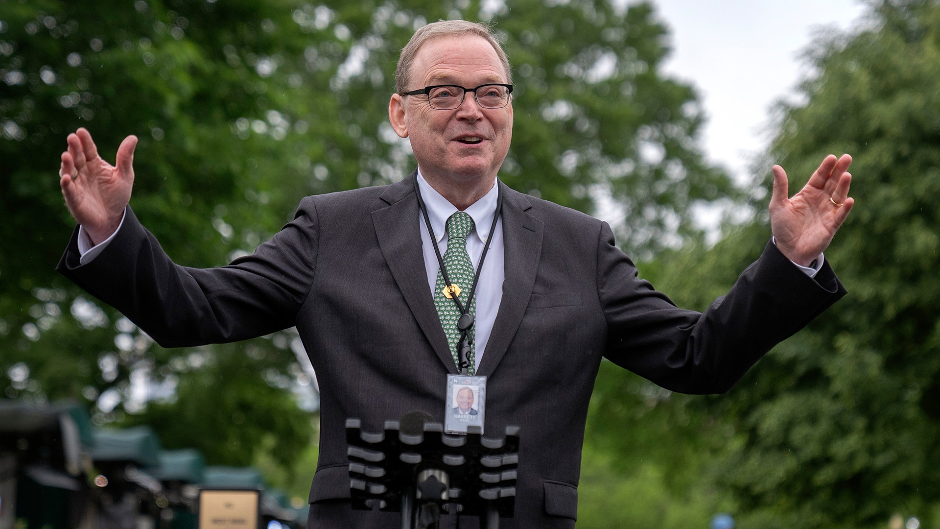 Kevin Hassett står glad vid en talarstol utomhus. Han sträcker ut händerna och ler till publiken.