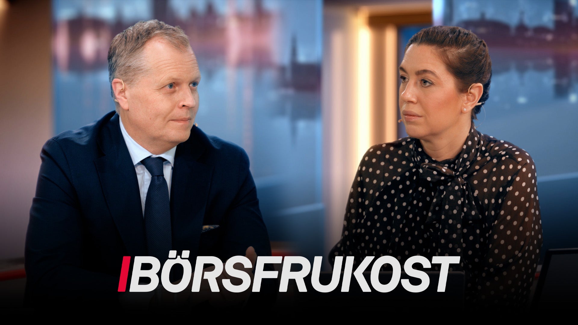 En man och en kvinna i en professionell intervjusituation med stadssilhuett i bakgrunden.