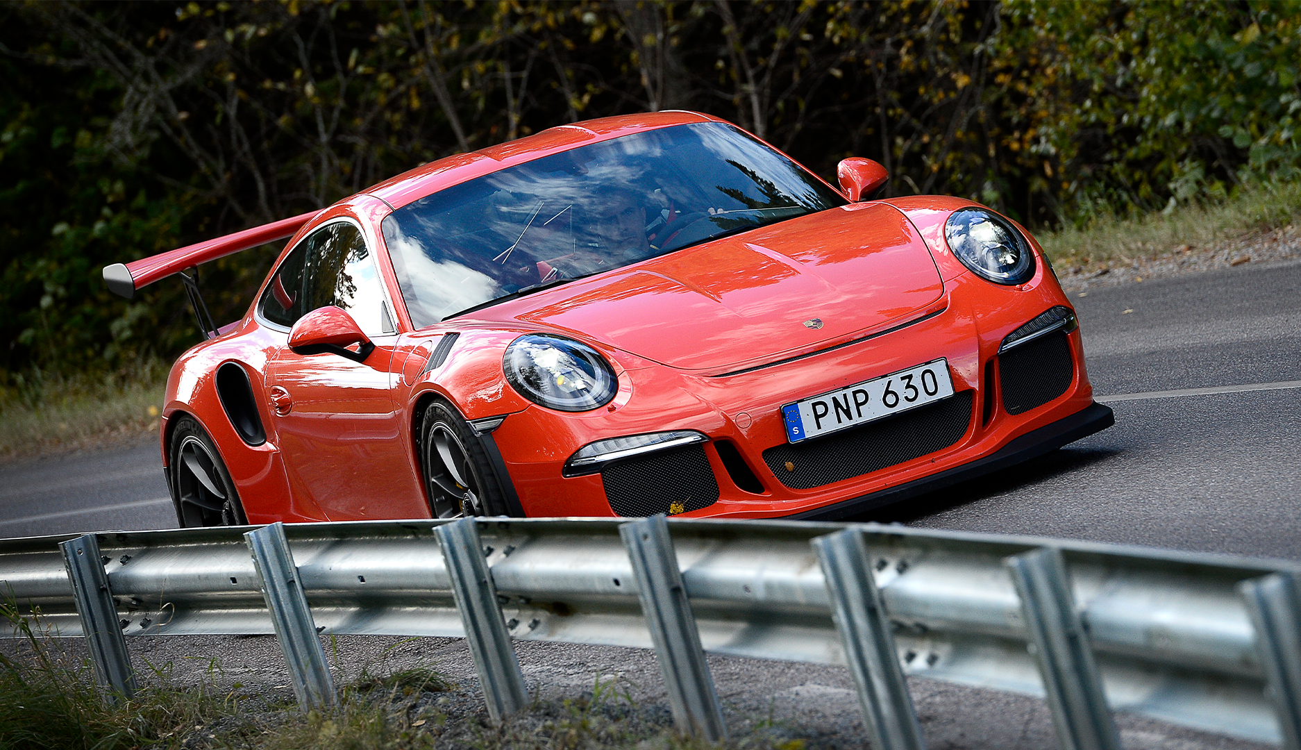 En röd Porsche 911 kör på en landsväg.