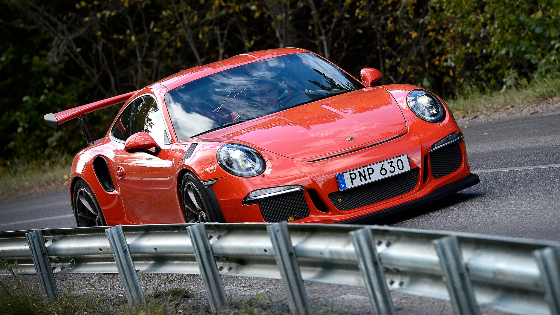 En röd Porsche 911 kör på en landsväg.