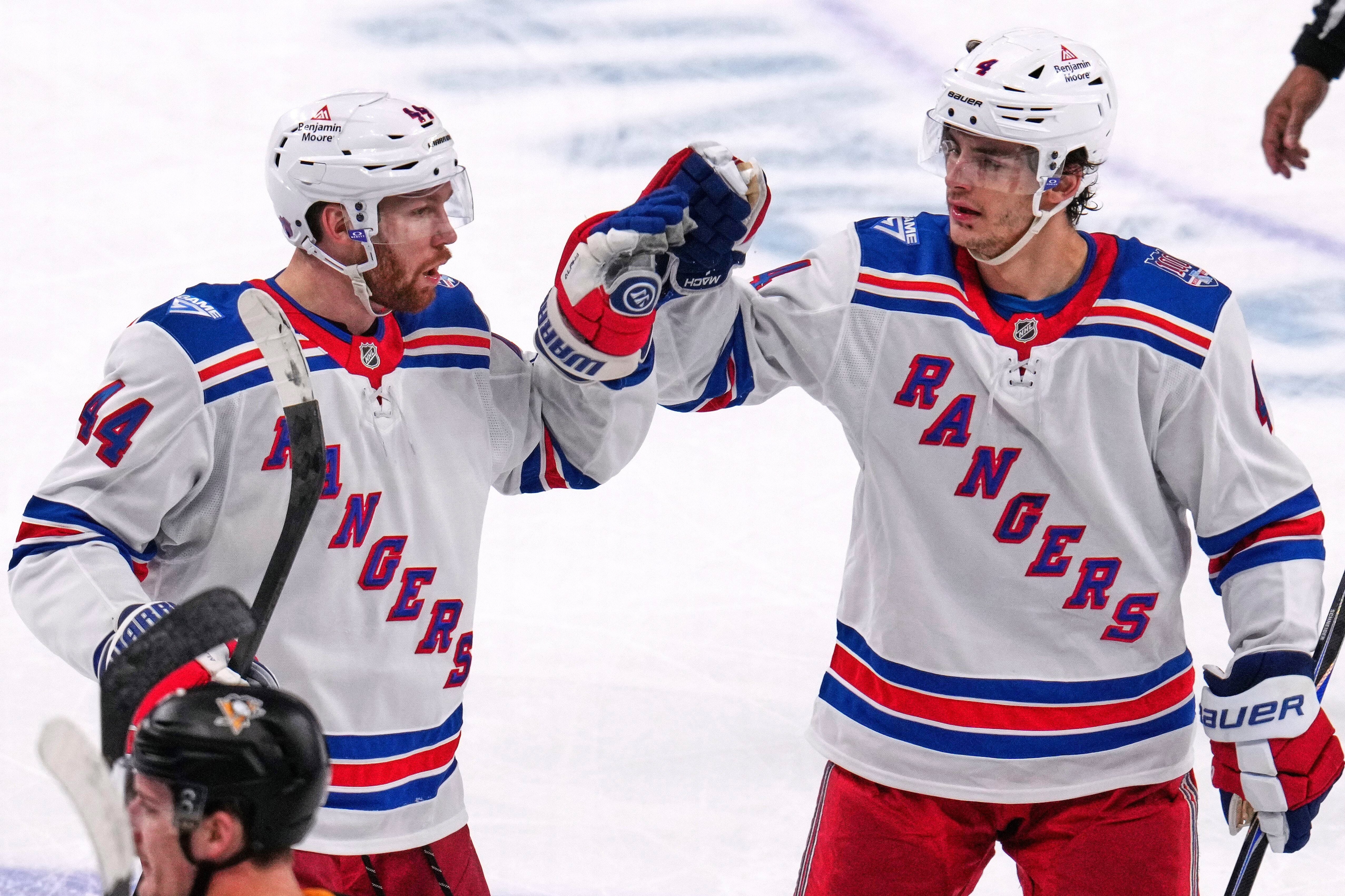 Två ishockeyspelare i New York Rangers vita tröjor ger varandra en high-five under en match.