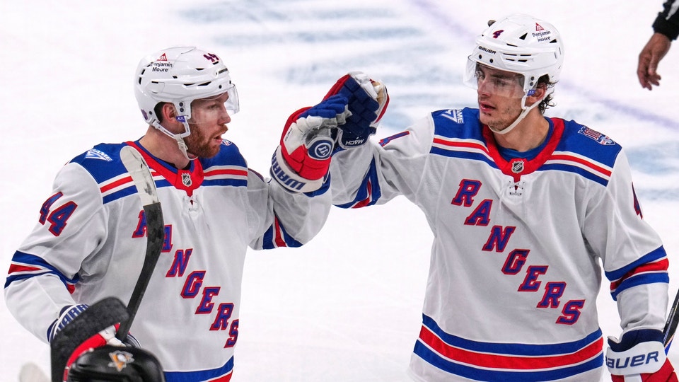 Två ishockeyspelare i New York Rangers vita tröjor ger varandra en high-five under en match.