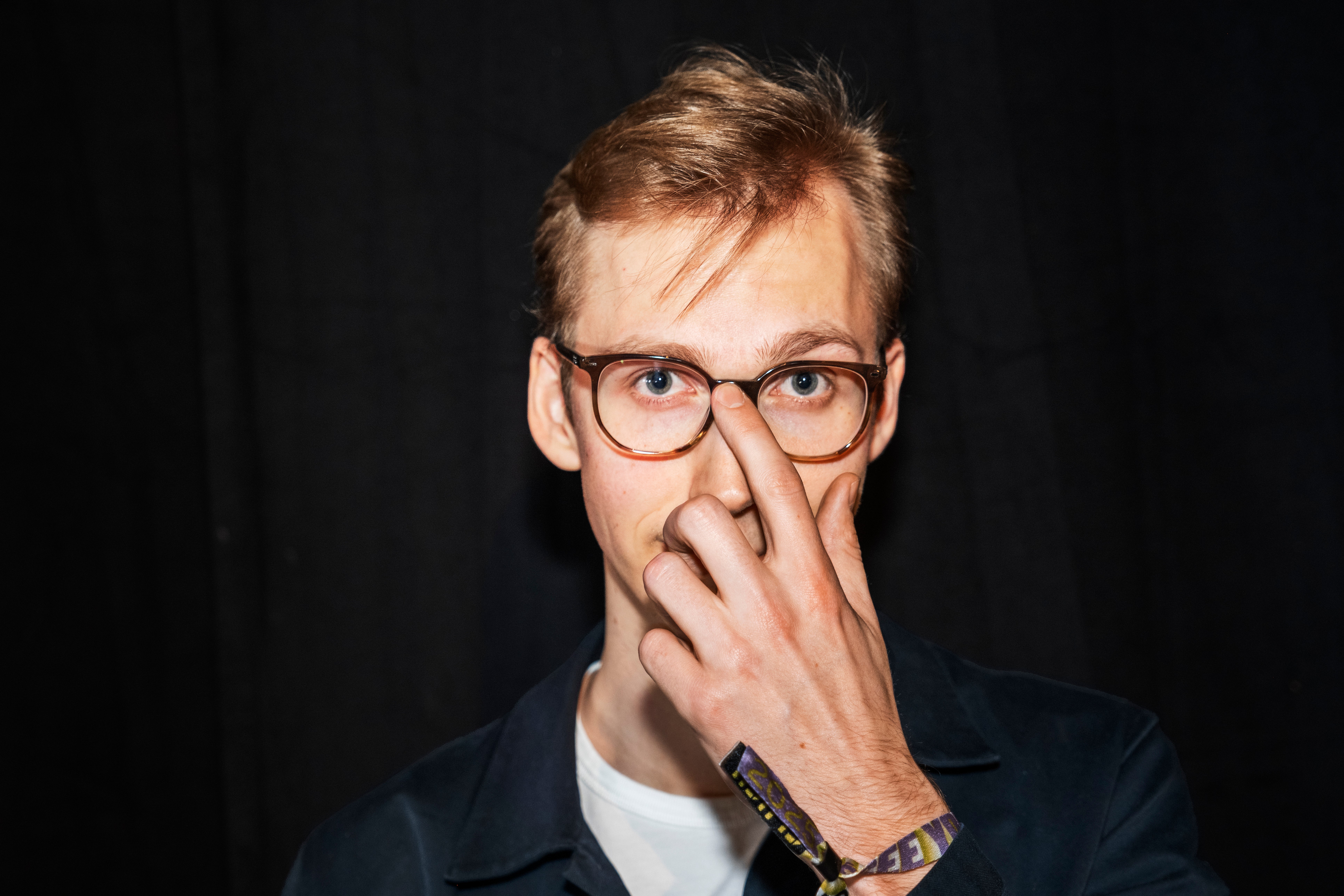 Person med glasögon som håller handen mot ansiktet i en tankfull pose mot mörk bakgrund