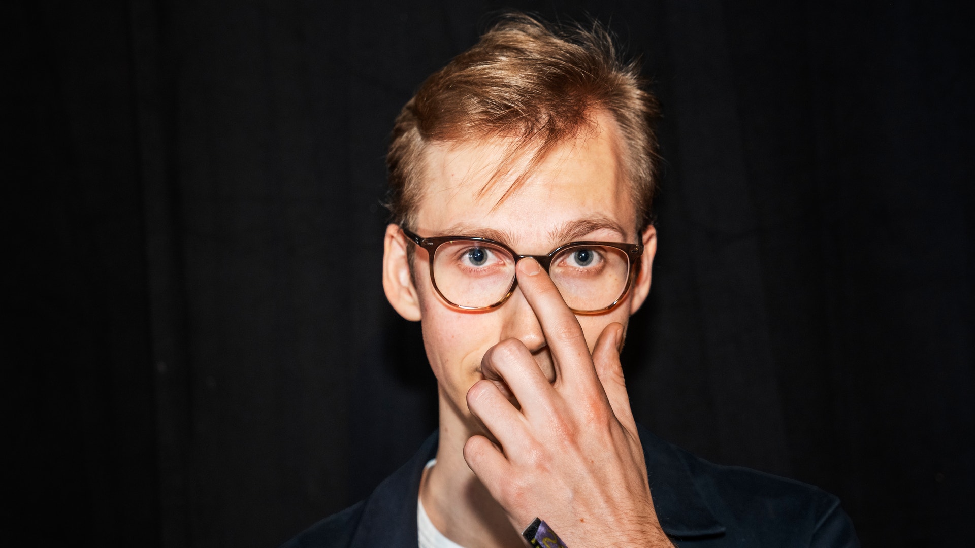 Person med glasögon som håller handen mot ansiktet i en tankfull pose mot mörk bakgrund