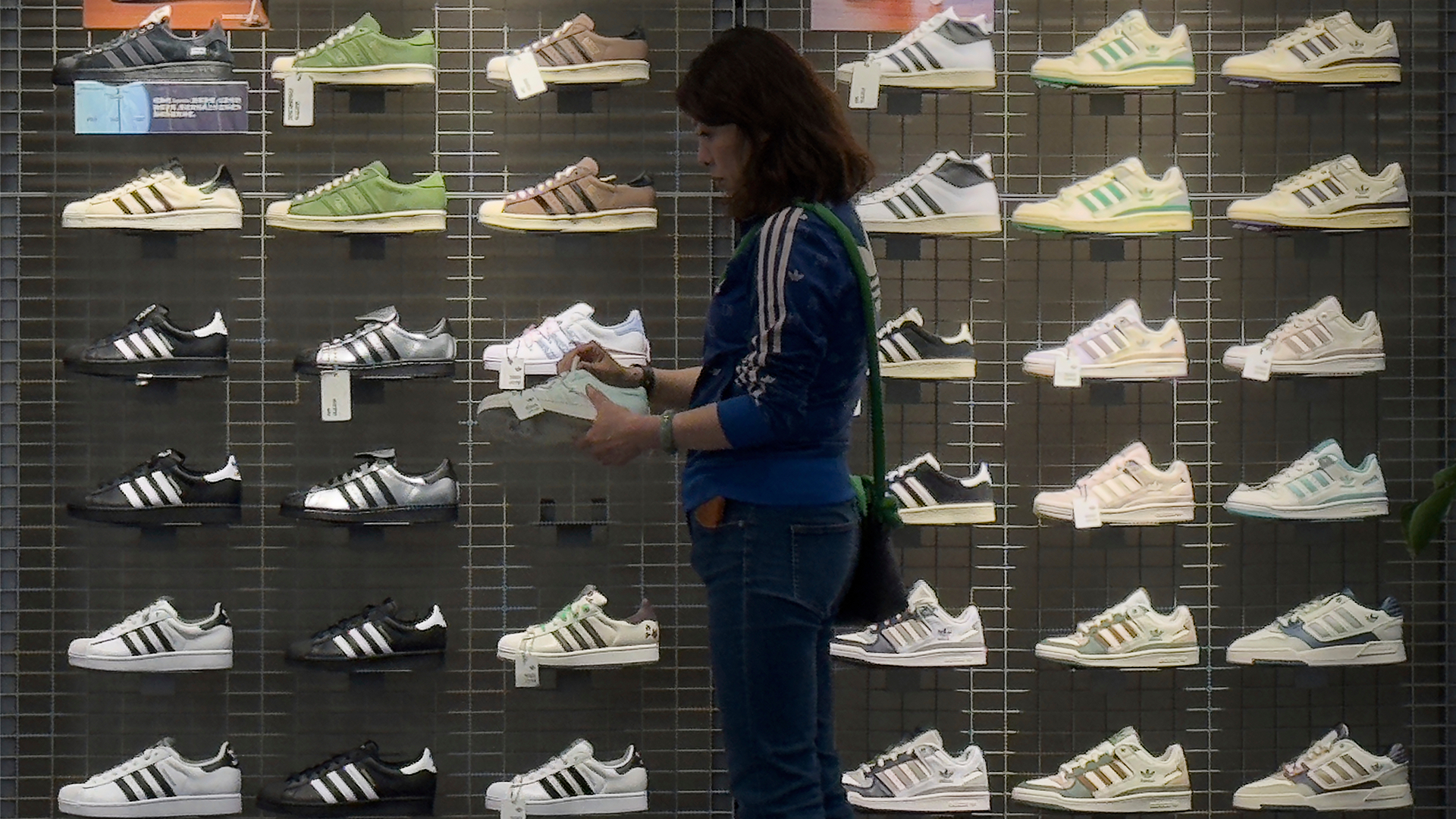 Person i blå Adidas-träningsoverall tittar på skor som är utställda på en vägg i en skobutik.