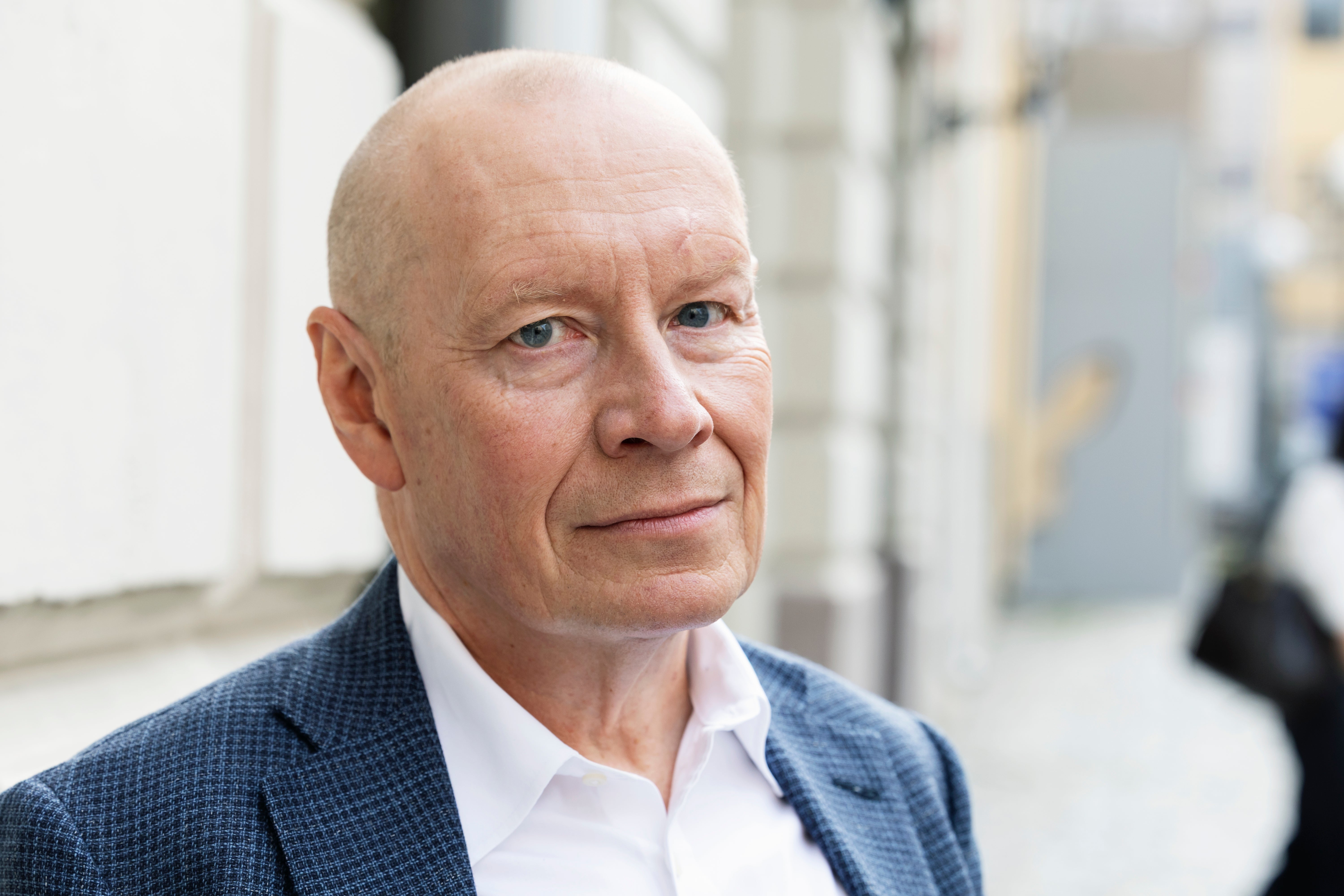 Porträtt av en äldre man i blå kavaj och vit skjorta, fotograferad utomhus.
