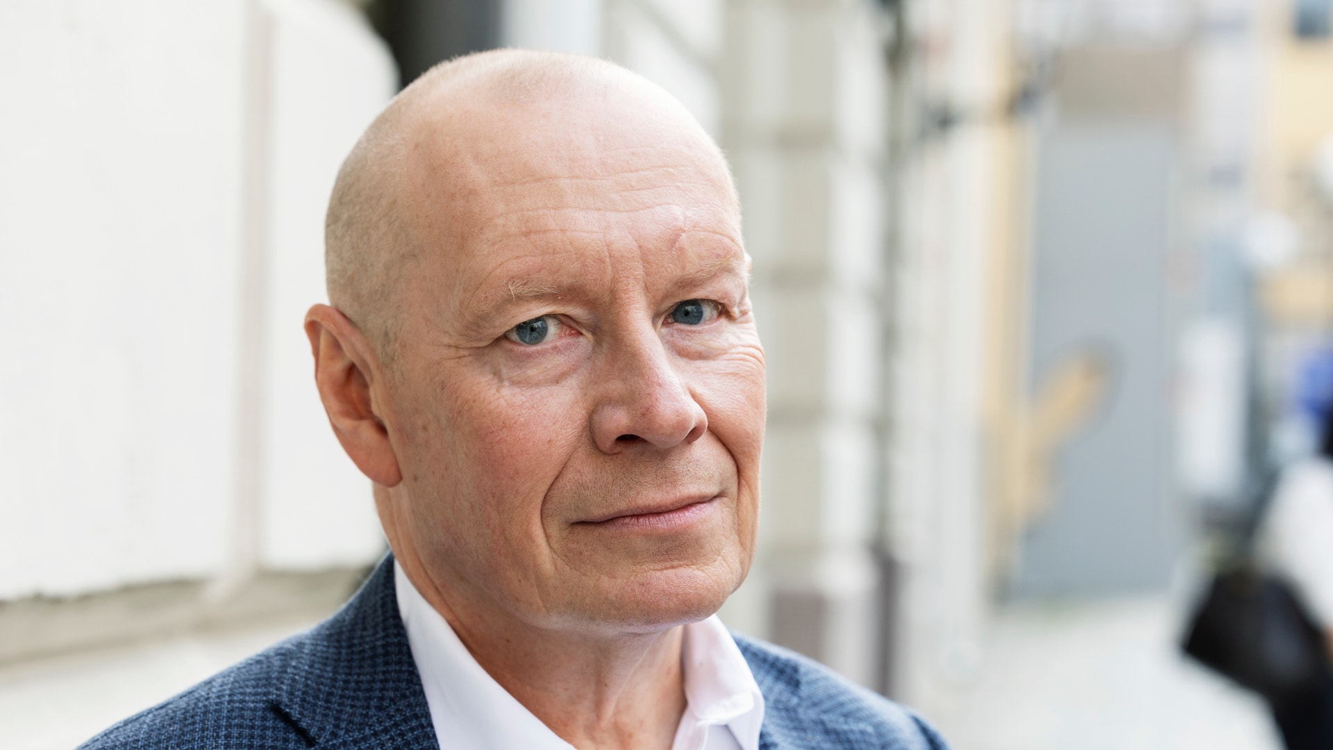 Porträtt av en äldre man i blå kavaj och vit skjorta, fotograferad utomhus.