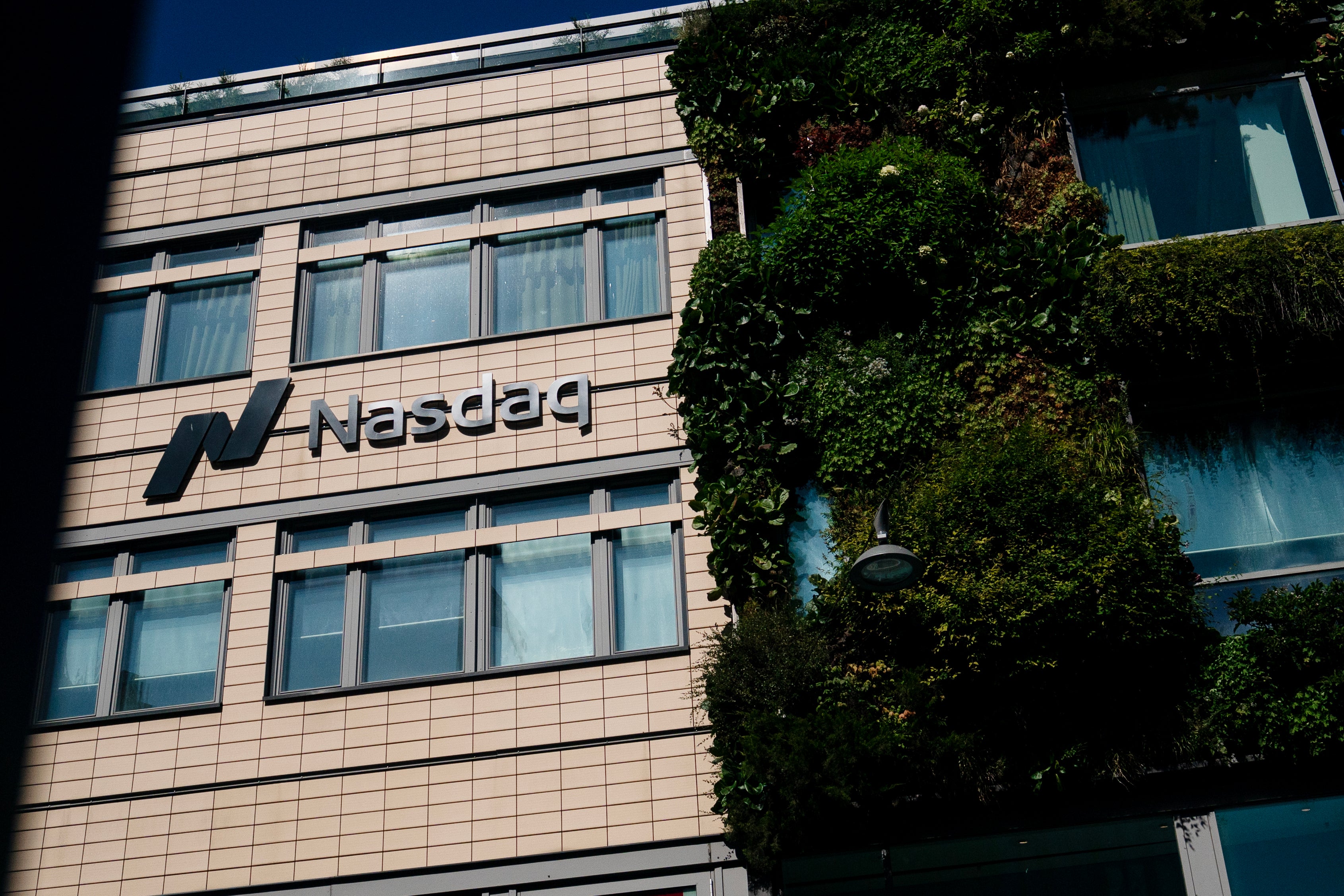 Fasad på Nasdaq-byggnad med beige tegelfasad, flera fönster och grön växtvägg på höger sida.