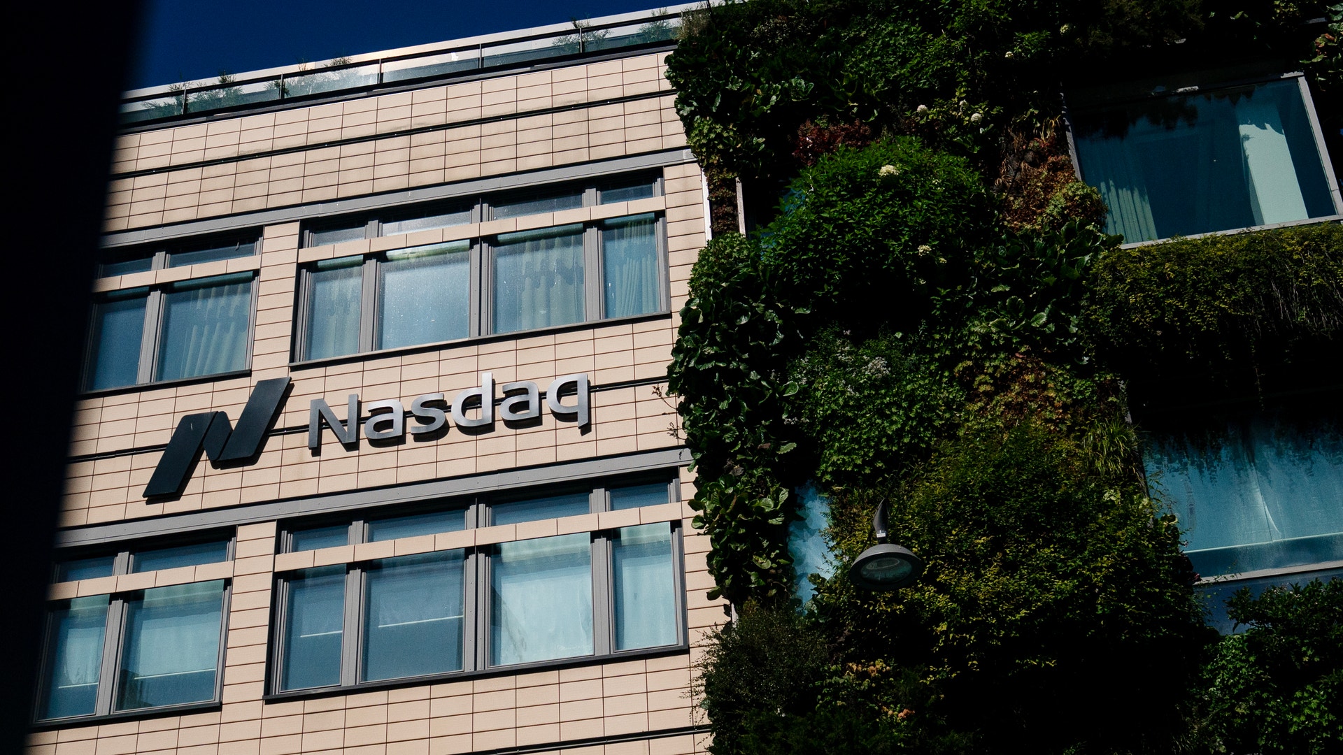 Fasad på Nasdaq-byggnad med beige tegelfasad, flera fönster och grön växtvägg på höger sida.